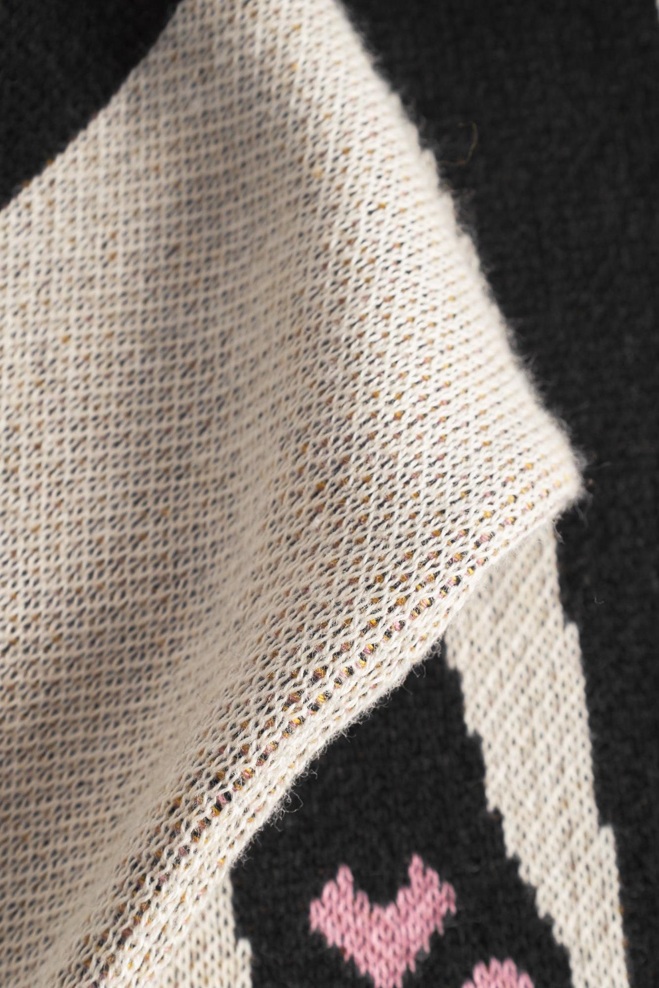 Close-up of a knit fabric with a black and cream geometric pattern and small pink heart details.