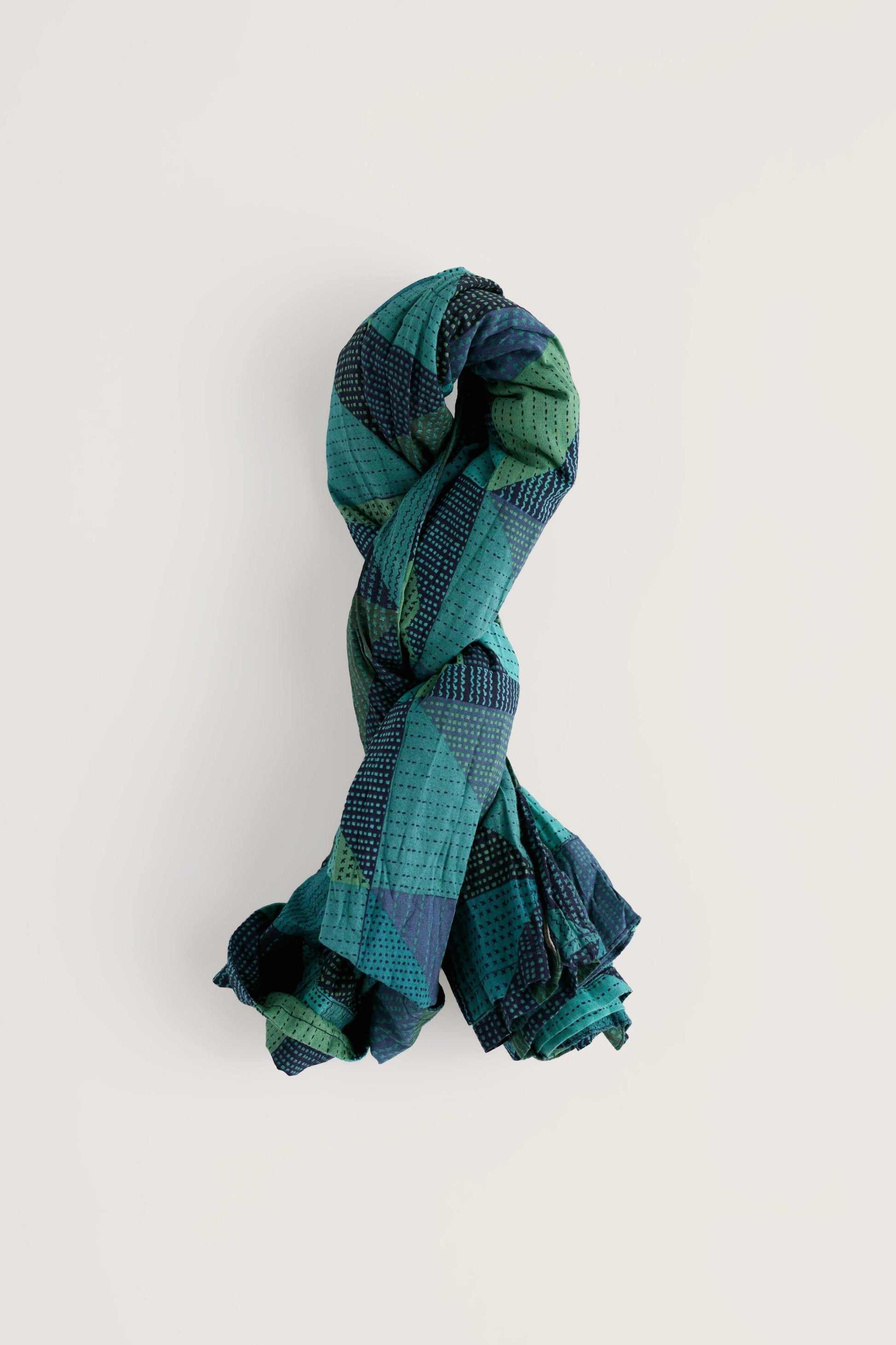 A folded shirt in shades of teal, green, and navy blue, presented on a clean off-white background.