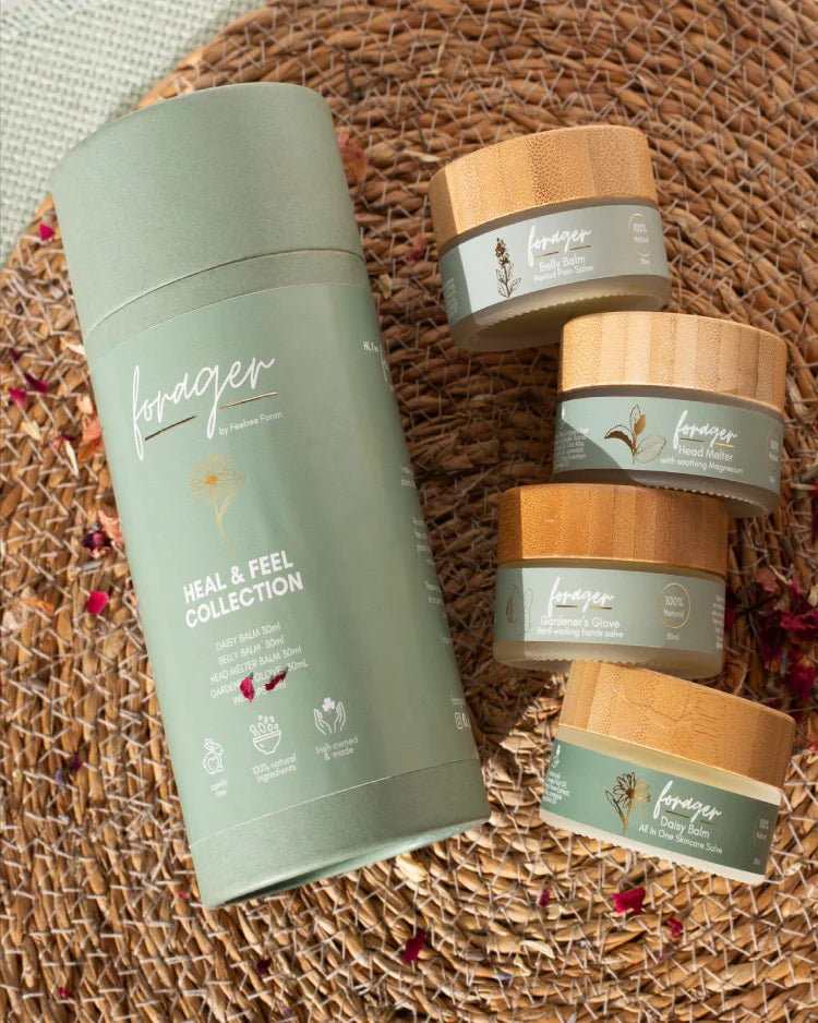 Forager Heal & Feel skincare collection including balm tubes and jars on a woven mat with dried flower petals.