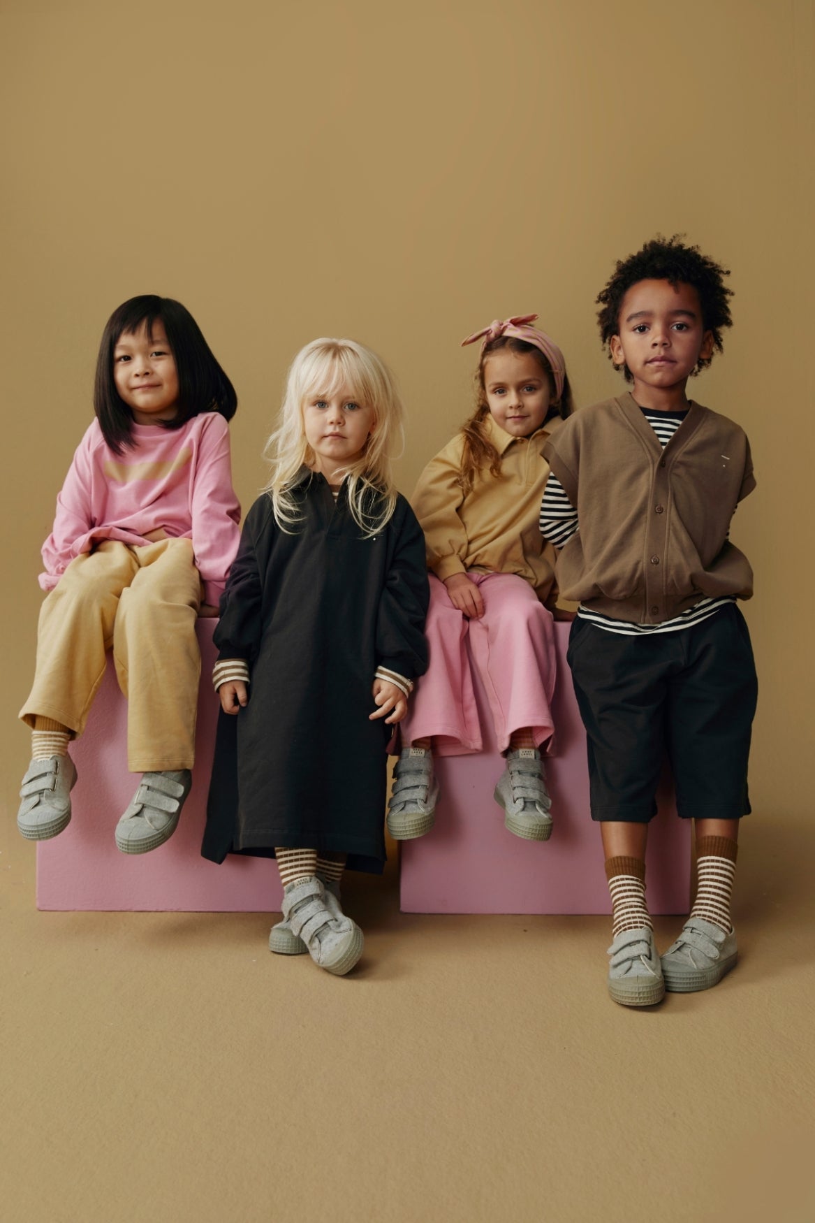 Four children sitting on a pink platform against a beige background