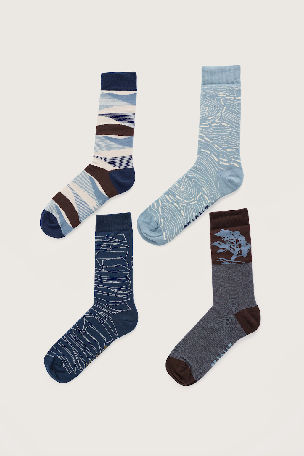 Four pairs of patterned crew socks arranged on a light beige background. The socks feature abstract wavy stripe designs in navy, blue, brown, and cream, as well as textured wave and tree-like graphic prints in navy, light blue, and dark gray.