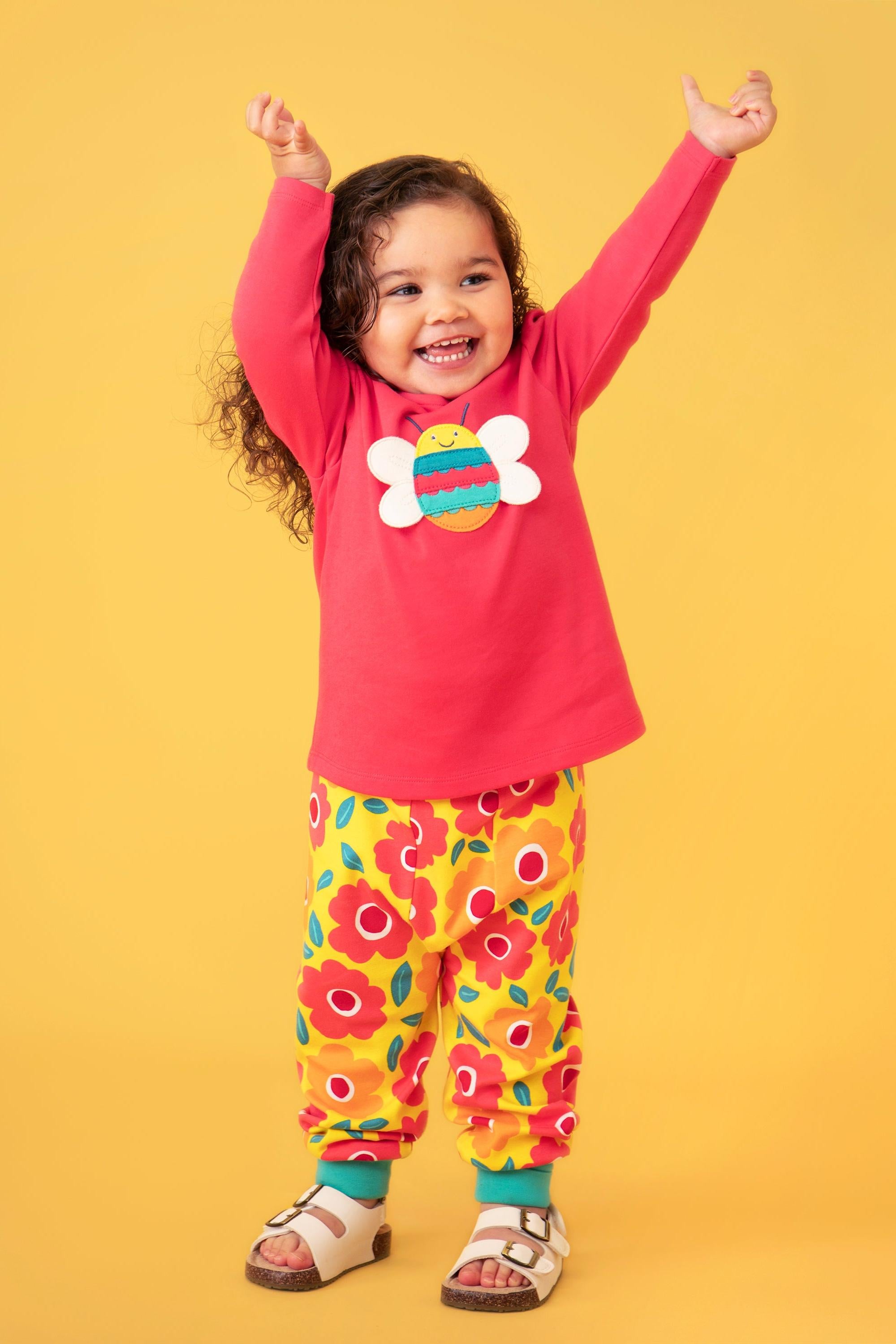 Child wearing a pink organic cotton shirt with a colorful design and yellow floral pants on a yellow background