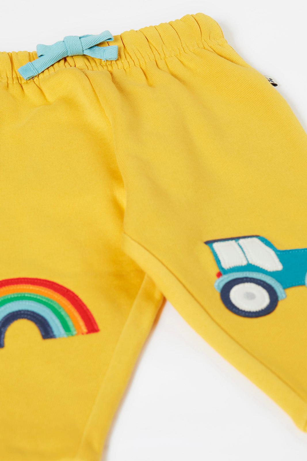 Yellow organic cotton pants with rainbow and tractor designs on a white background