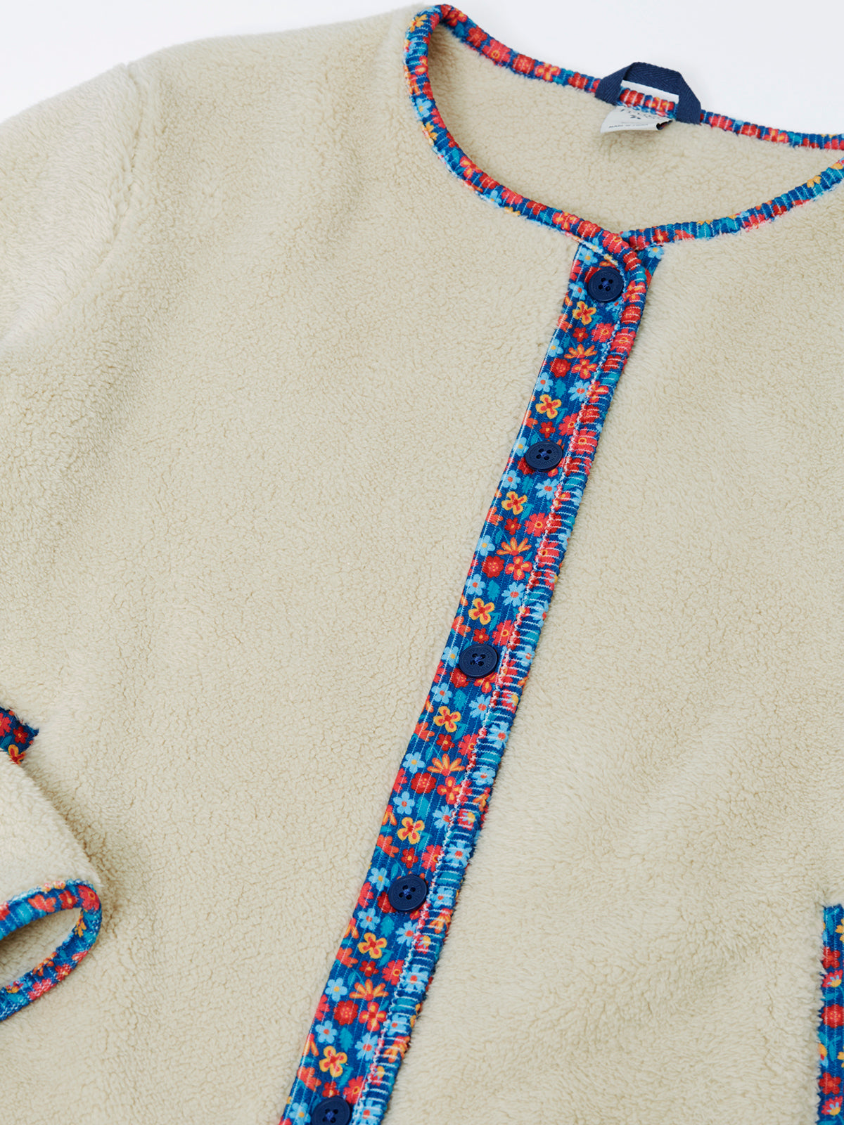 Close-up of a cream-colored Frugi girls fleece jacket with colorful floral trim and blue buttons.