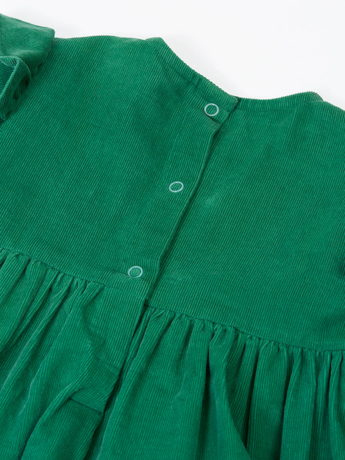 Close up of a green organic cotton corduroy baby dress with back button closure details.