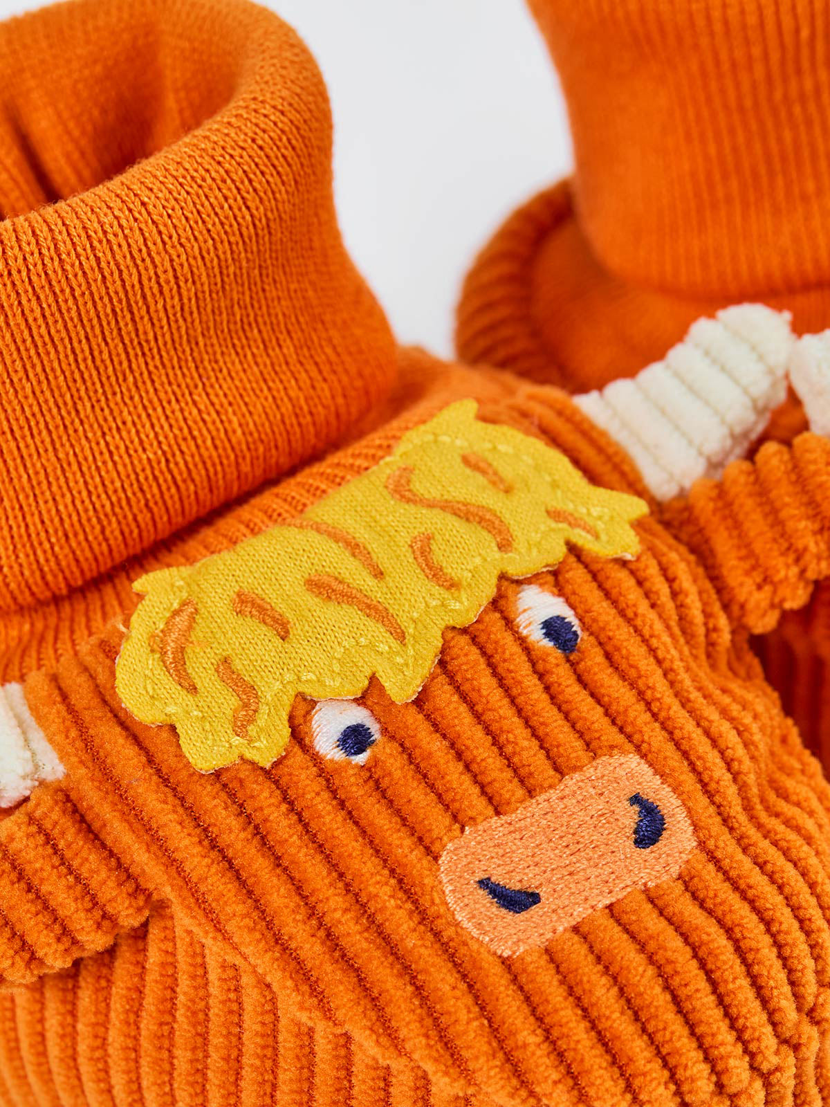 Close-up of Frugi orange baby booties featuring a cute embroidered highland cow design made from recycled material.