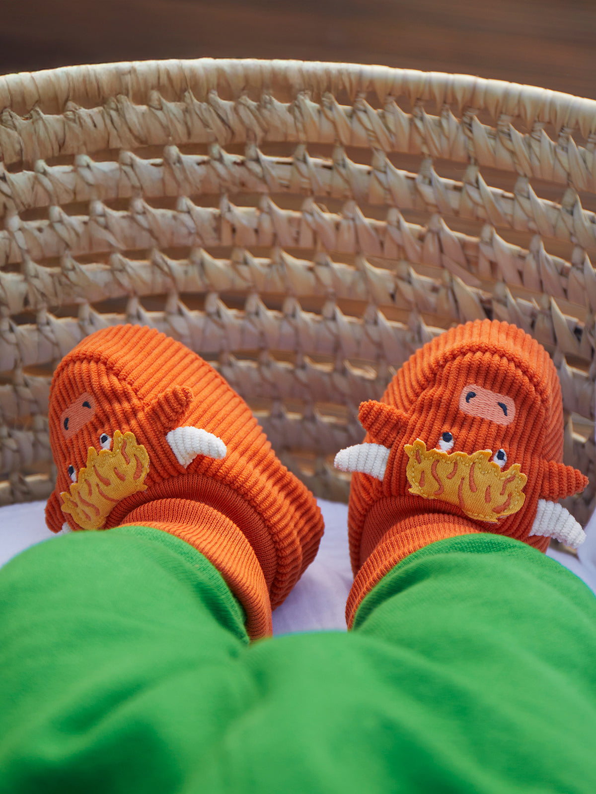 A pair of orange Frugi baby booties featuring a cute highland cow design worn on a baby's feet.