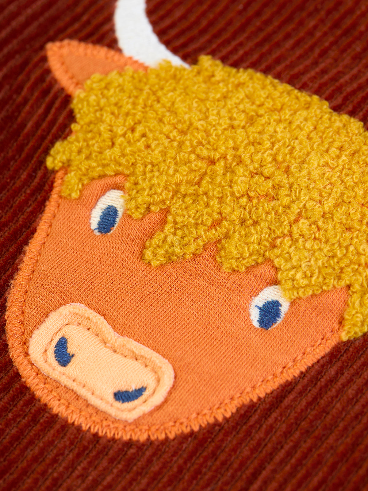 Close up of a Highland cow applique on brown Frugi organic cotton corduroy trousers.