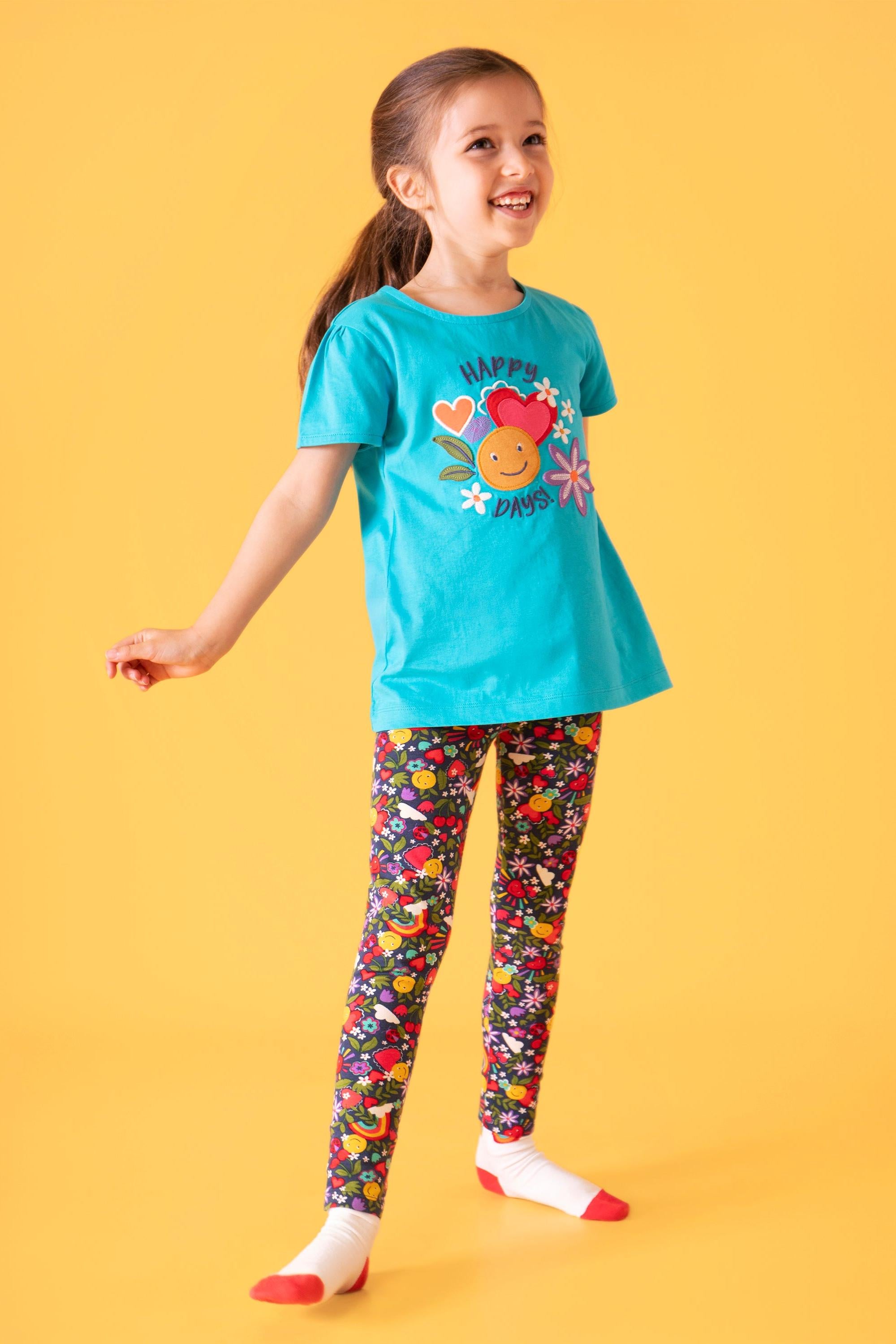 Young girl wearing a blue t-shirt with a cartoon character and colorful leggings on a yellow background