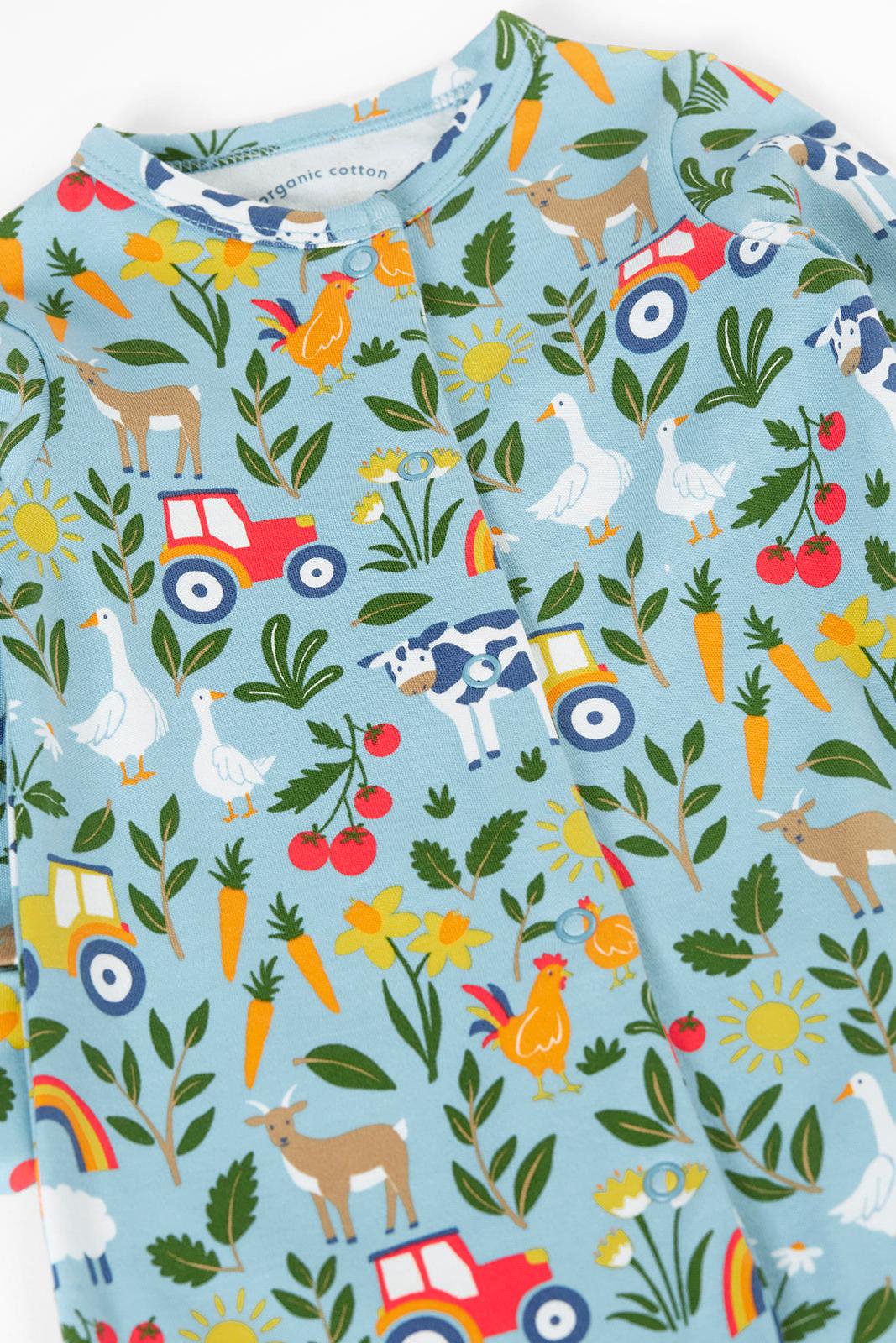 Children's babygrow with farm-themed pattern including animals, vehicles, and plants on a blue background.