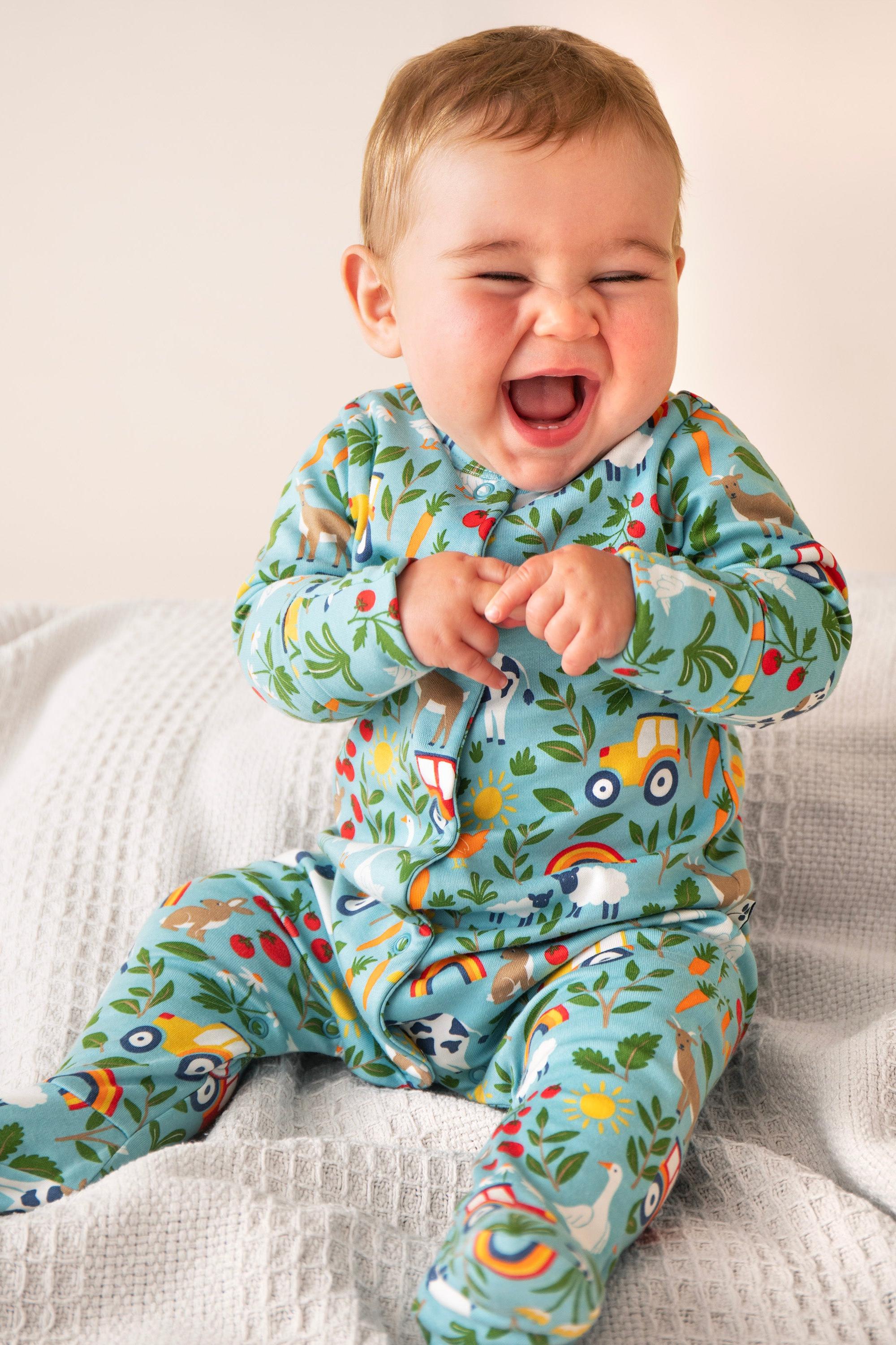 Baby wearing a colorful organic cotton onesie with farm pattern on a light background