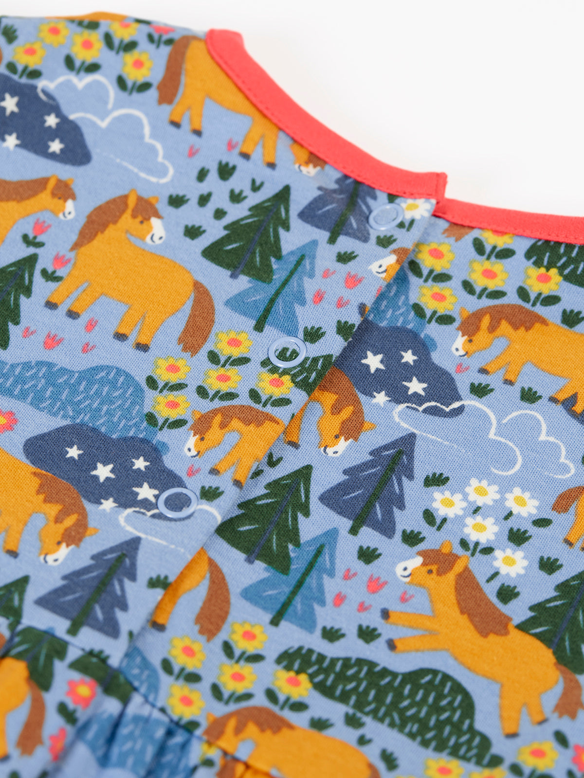 Close-up of a Frugi organic cotton baby dress featuring a colourful horse, flower, and forest pattern with snap buttons.