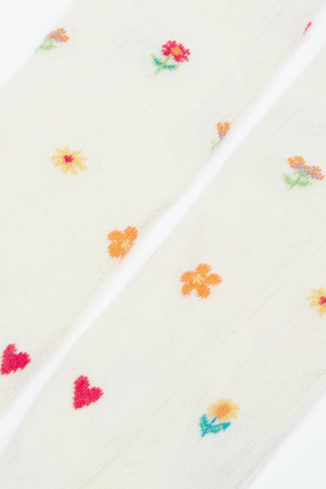Close-up of cream-colored Frugi organic cotton baby tights featuring colourful embroidered flowers and hearts.