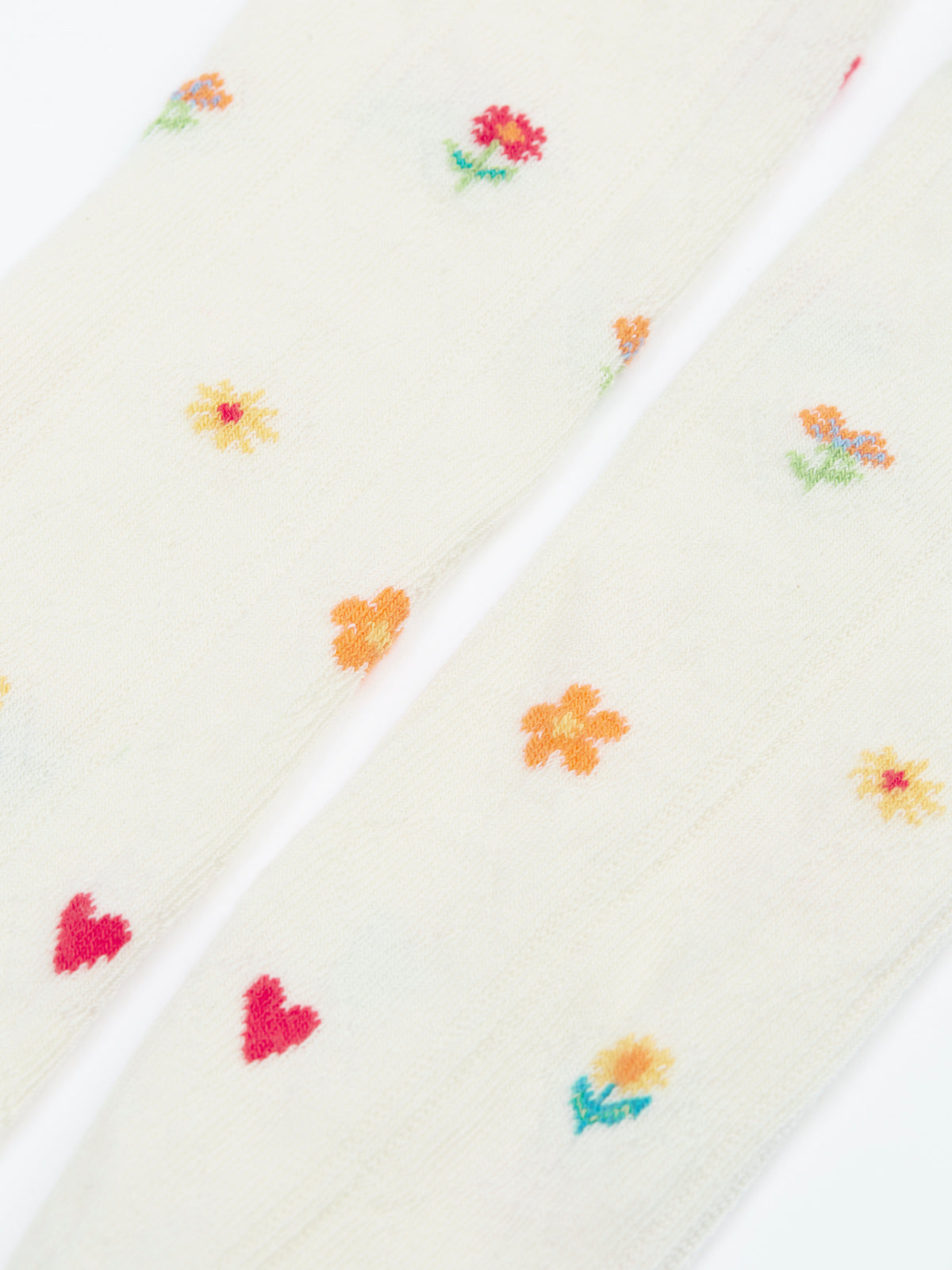 Close-up of cream-colored Frugi organic cotton baby tights featuring colourful embroidered flowers and hearts.