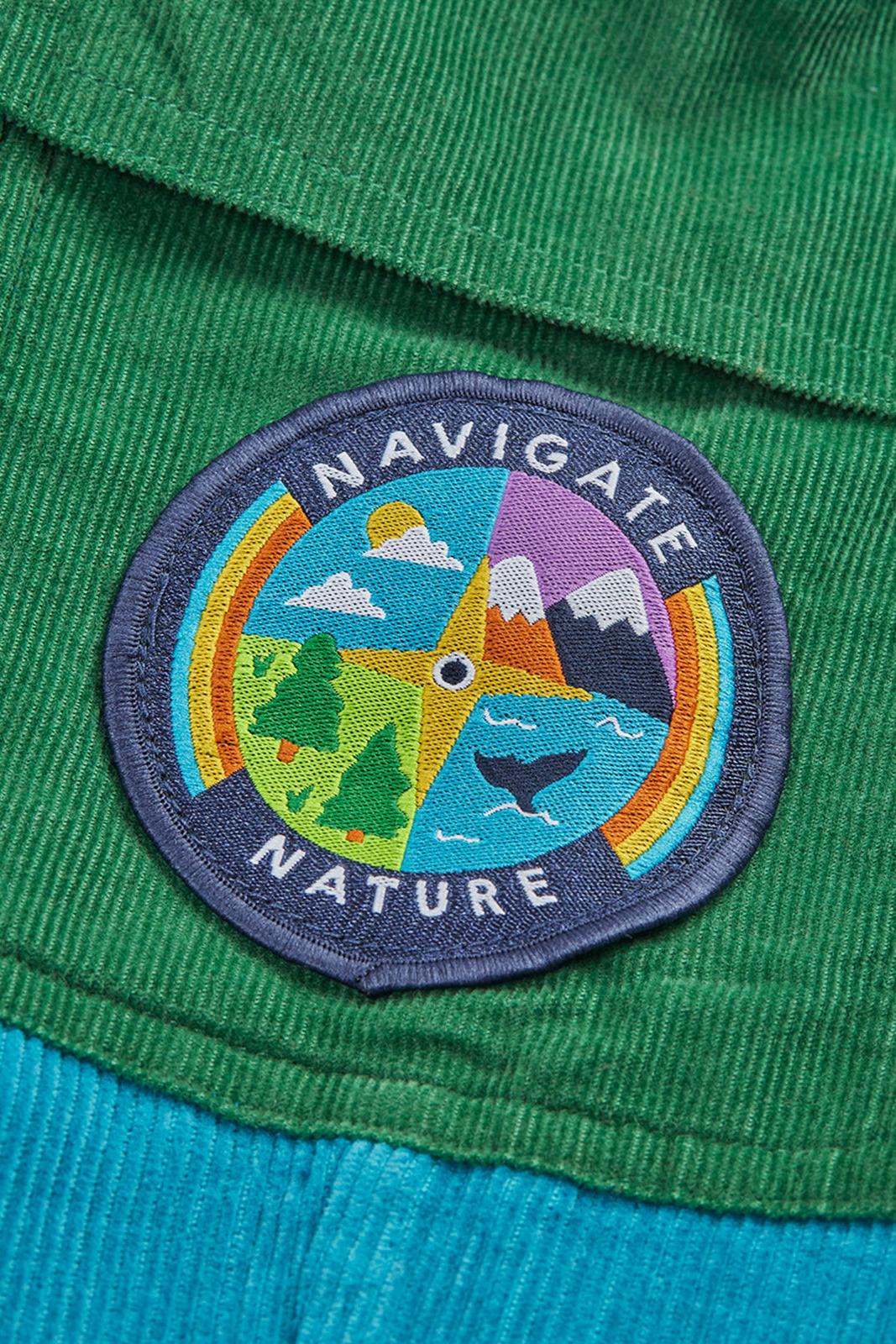 Close-up of a Navigate Nature circular embroidered patch on green organic cotton cord trousers.