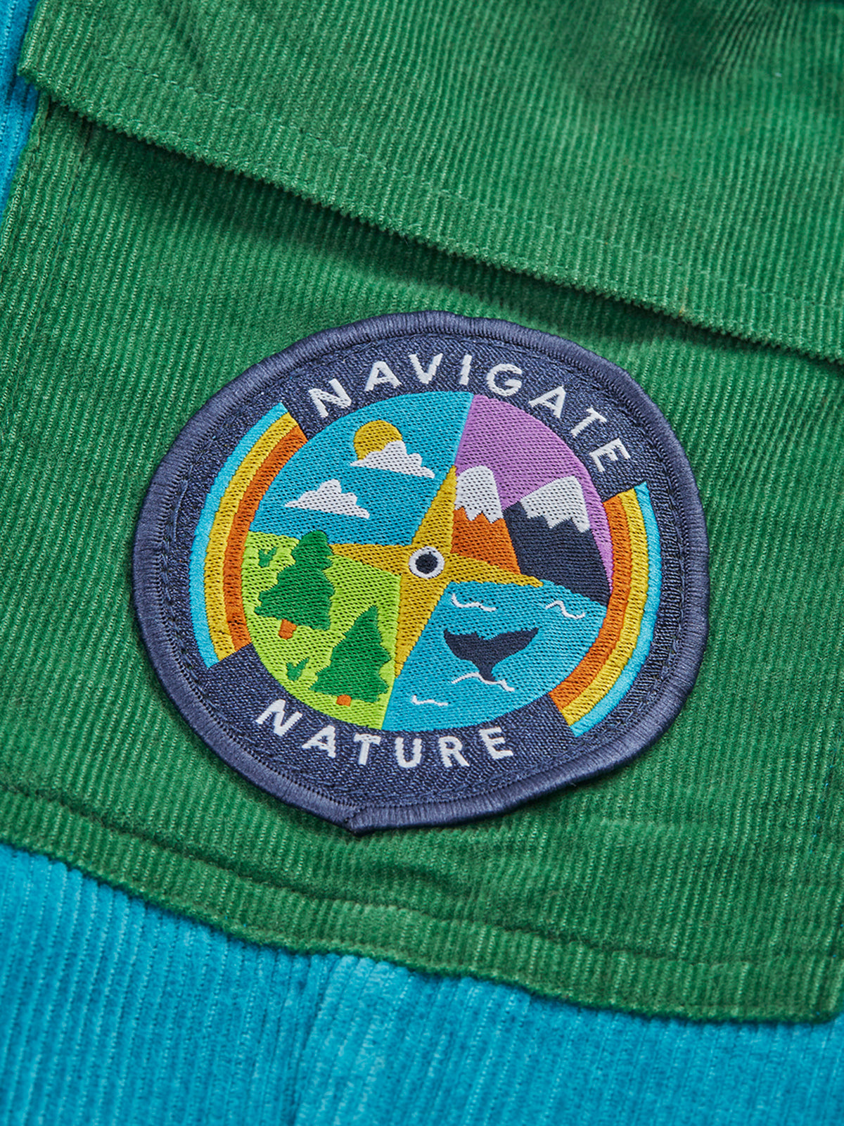 Close-up of a Navigate Nature circular embroidered patch on green organic cotton cord trousers.