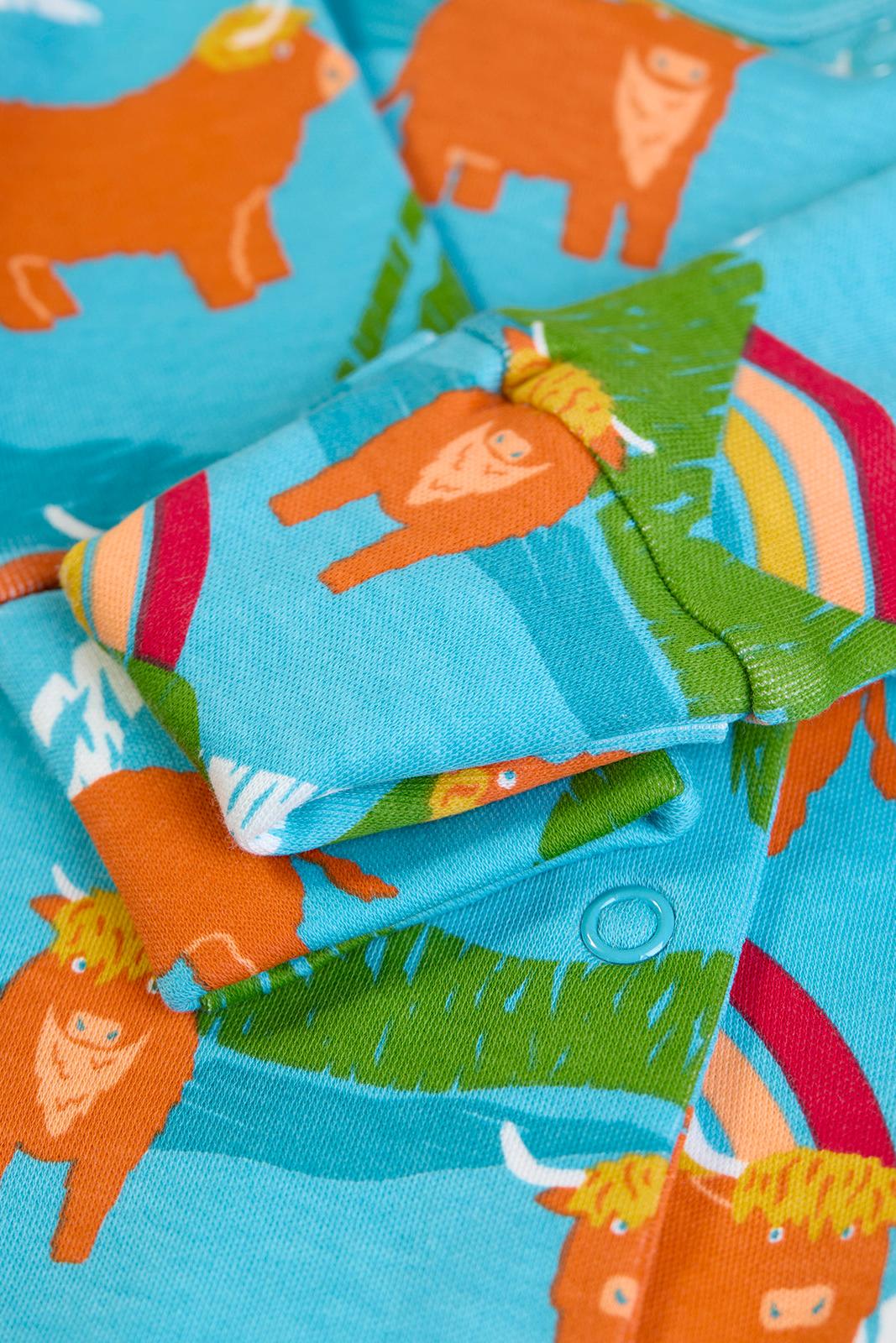 Close-up of a Frugi organic cotton babygro with a vibrant farm cow and rainbow print.