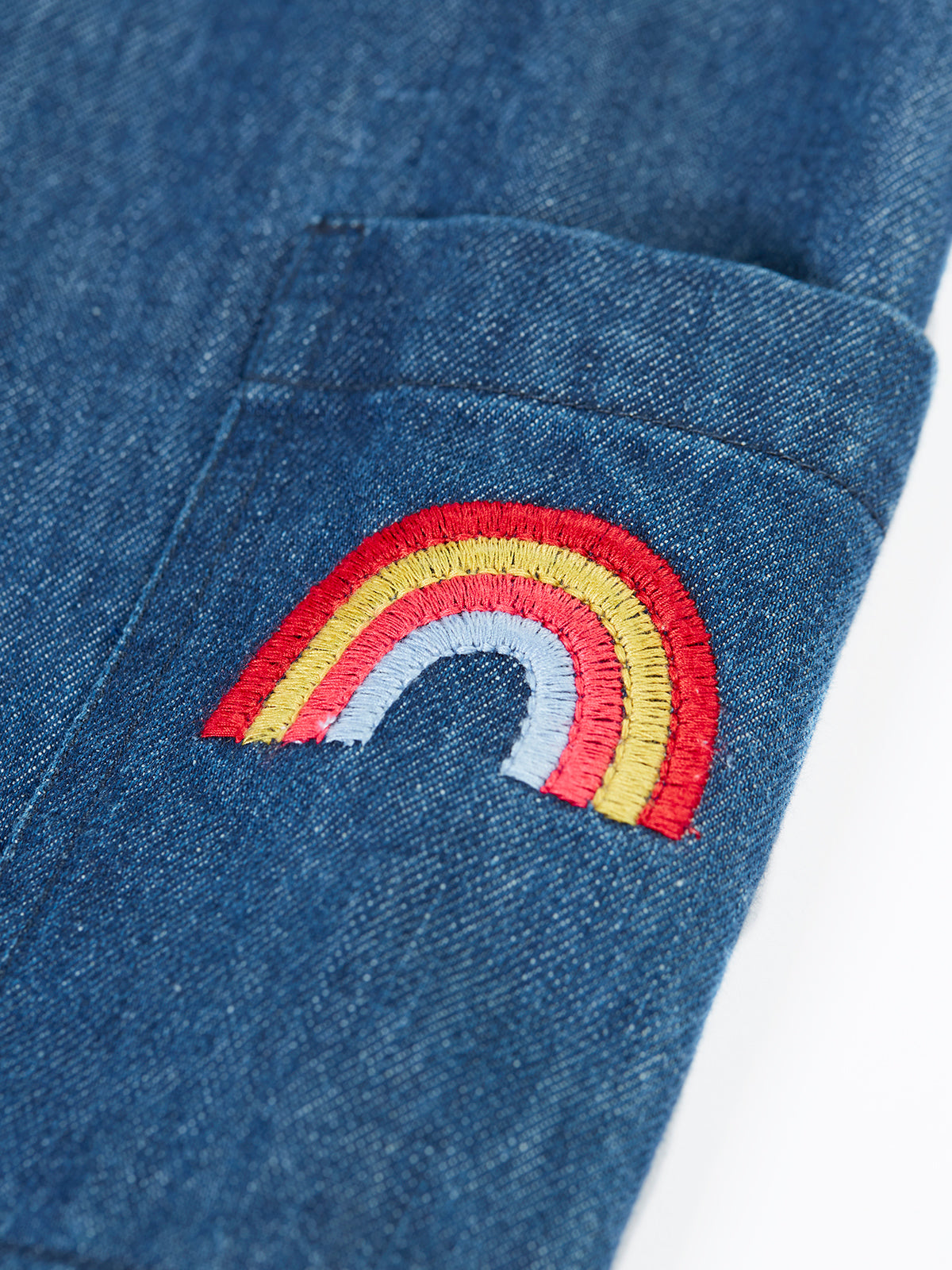 Close-up of a rainbow embroidery patch on a blue organic cotton denim jumpsuit.