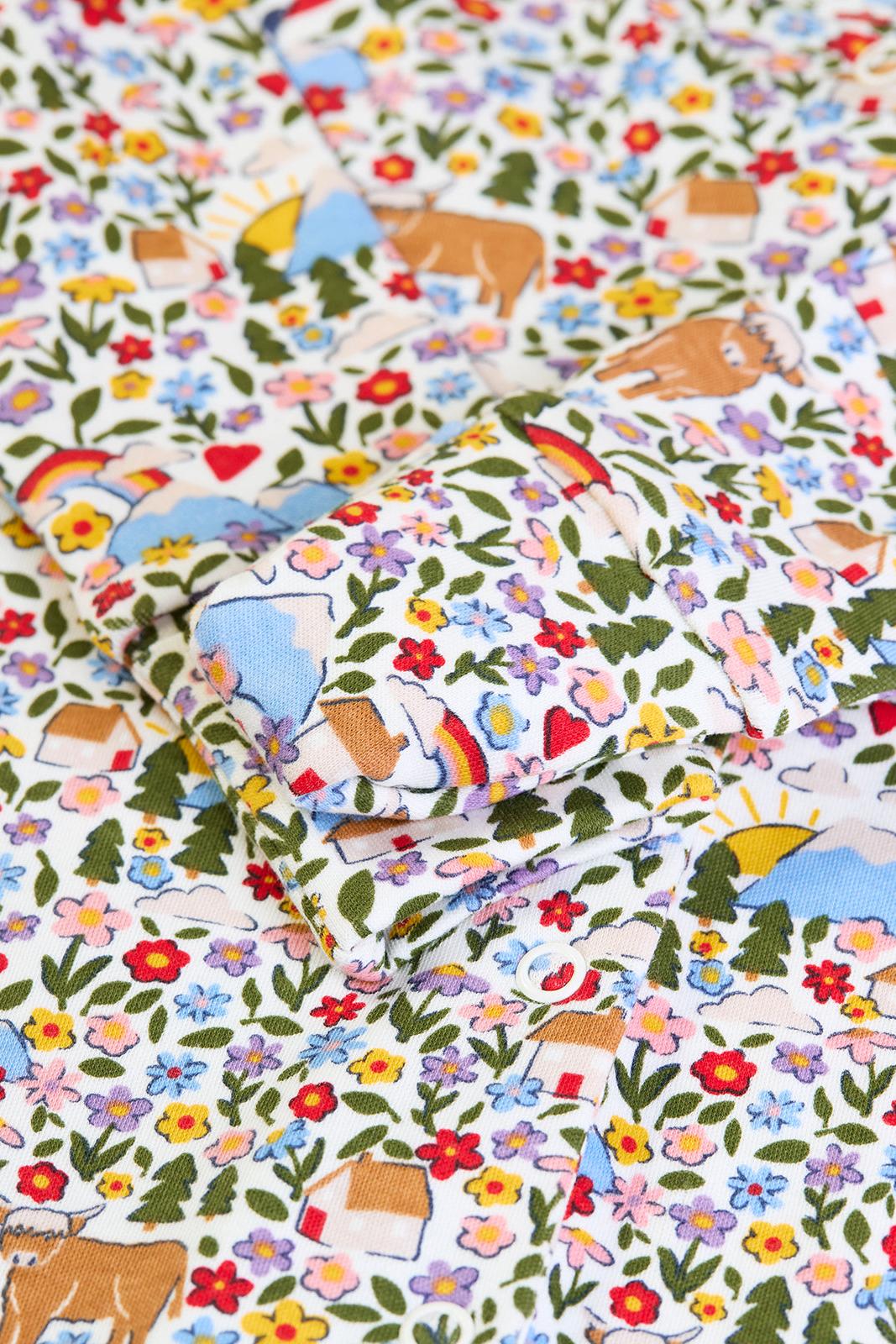 Close-up of a Frugi organic cotton babygro with a colorful floral, rainbow, and cow print pattern.