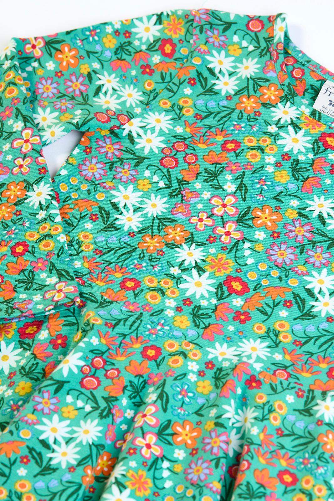 Close-up of a Frugi green organic cotton dress with a vibrant multi-colored floral pattern.