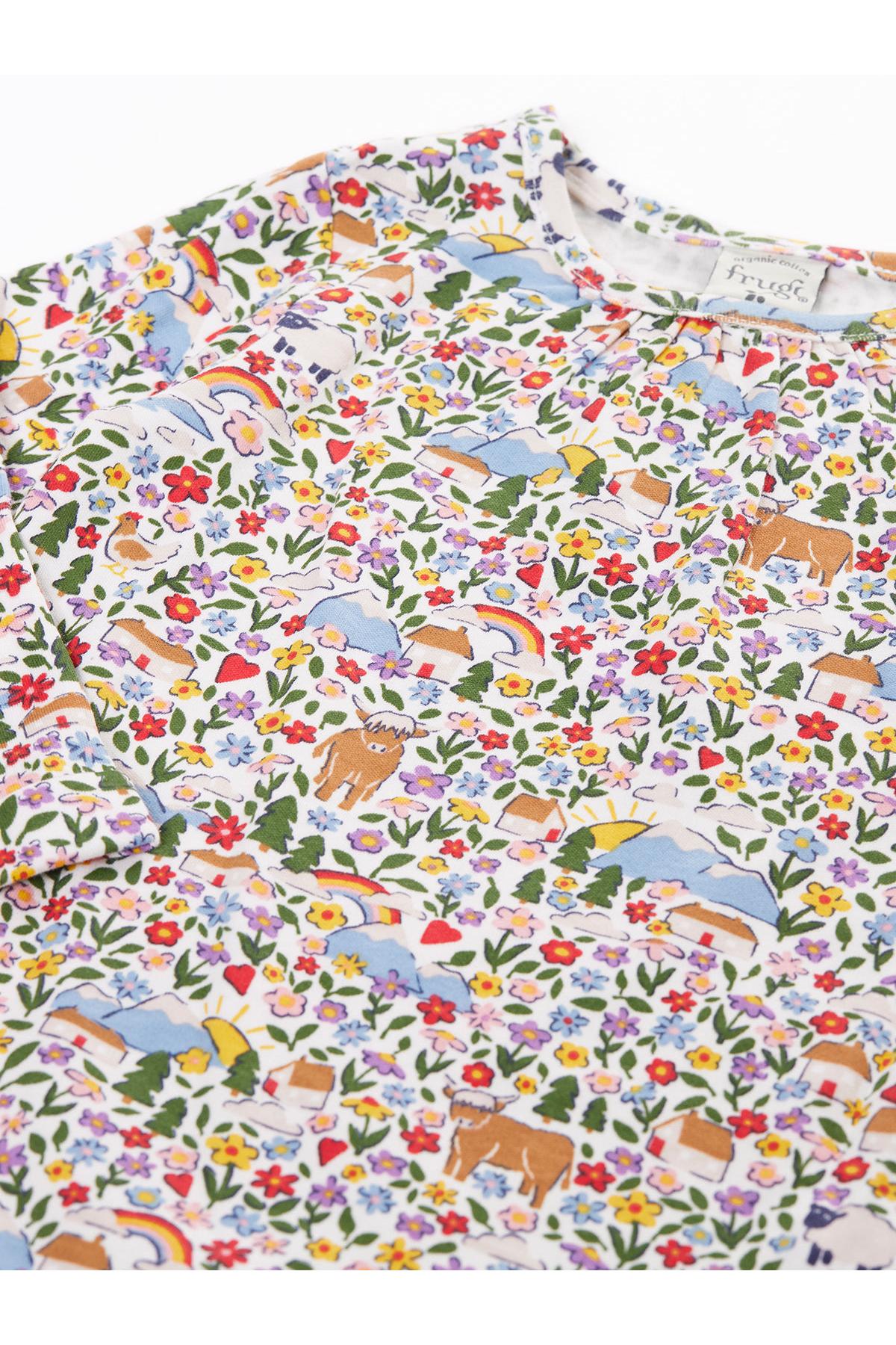 A close-up of a long-sleeve crewneck sweatshirt featuring a dense, colorful cartoon print. The pattern includes brown cows, blue mountains, yellow suns, red and blue flowers, green trees, and rainbows on a white background.
