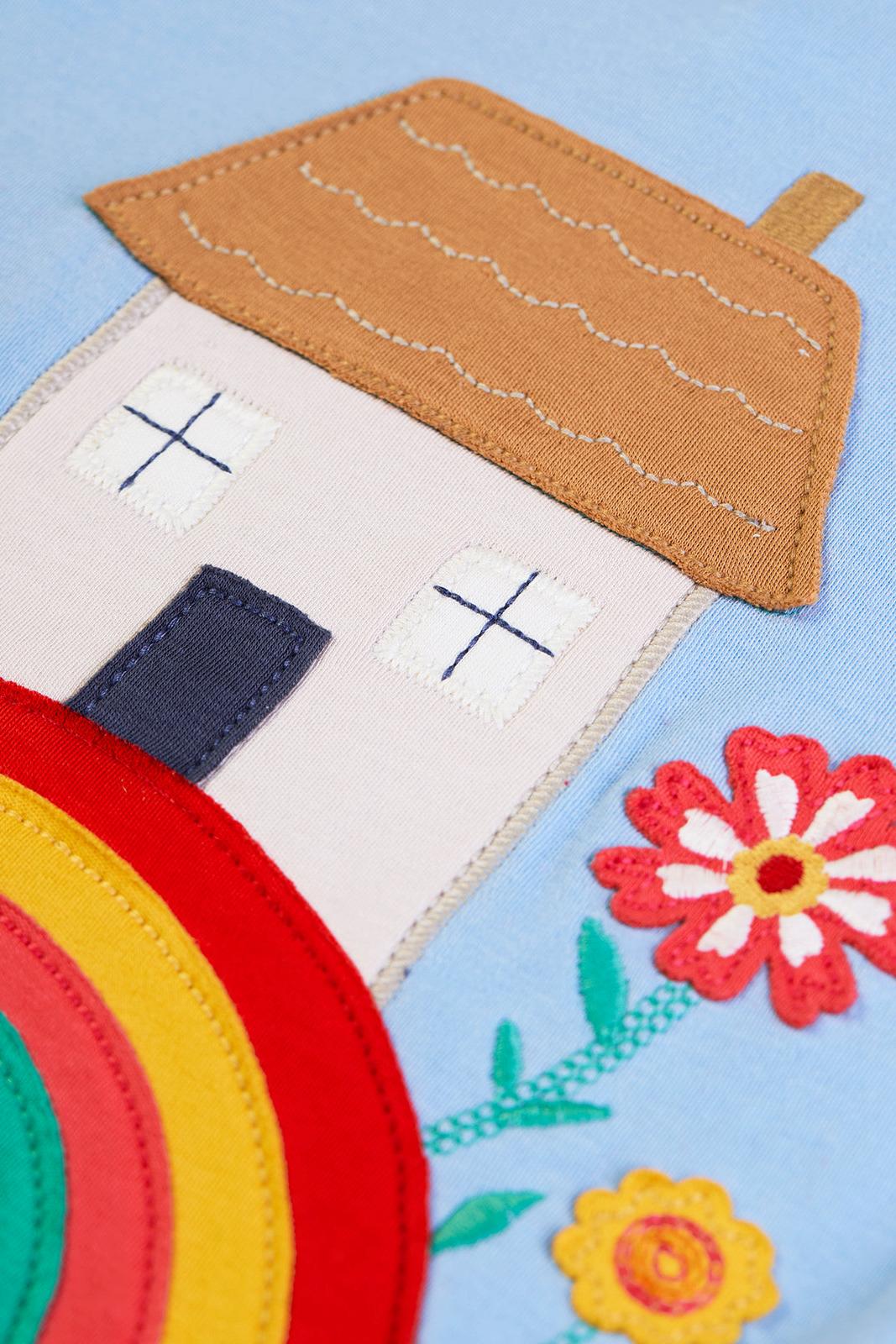 Close-up of a Frugi organic cotton girl's top with a colourful house and flower applique design on light blue fabric.