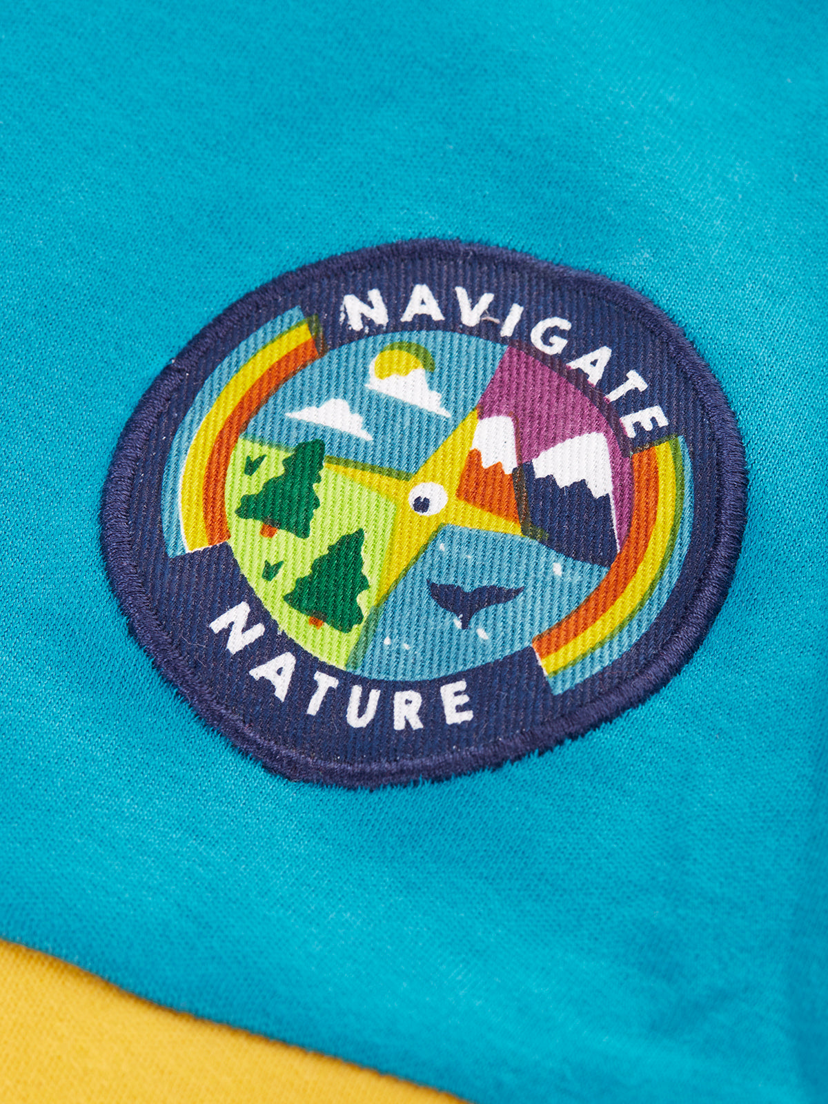 Close up of a Frugi organic cotton top featuring a colourful Navigate Nature circular embroidered patch.
