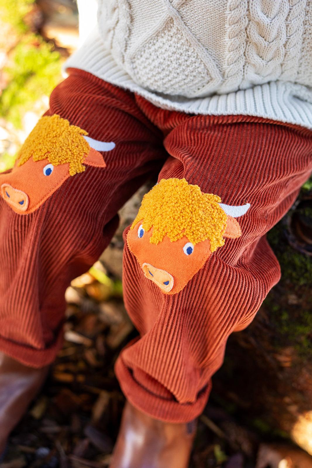 Child wearing brown organic cotton trousers with highland cow appliques on the knees