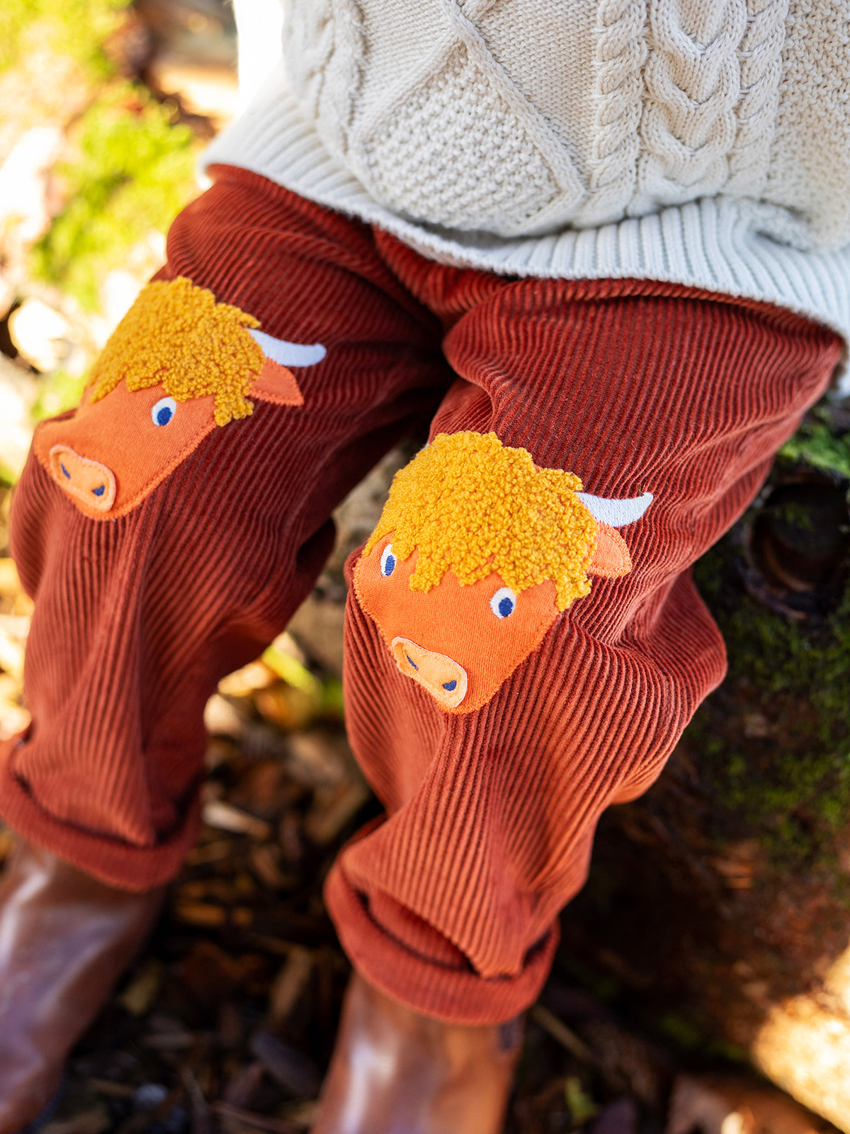 Child wearing brown organic cotton trousers with highland cow appliques on the knees