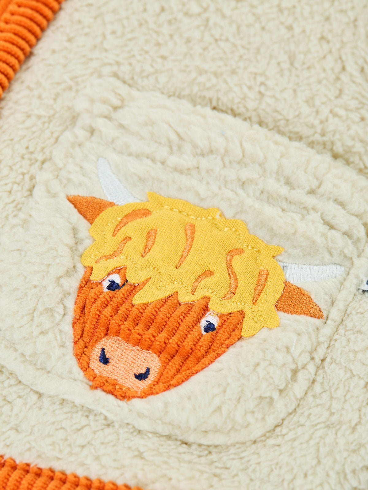 Close-up of a Frugi boys fleece jacket with a detailed embroidered highland cow pocket patch.