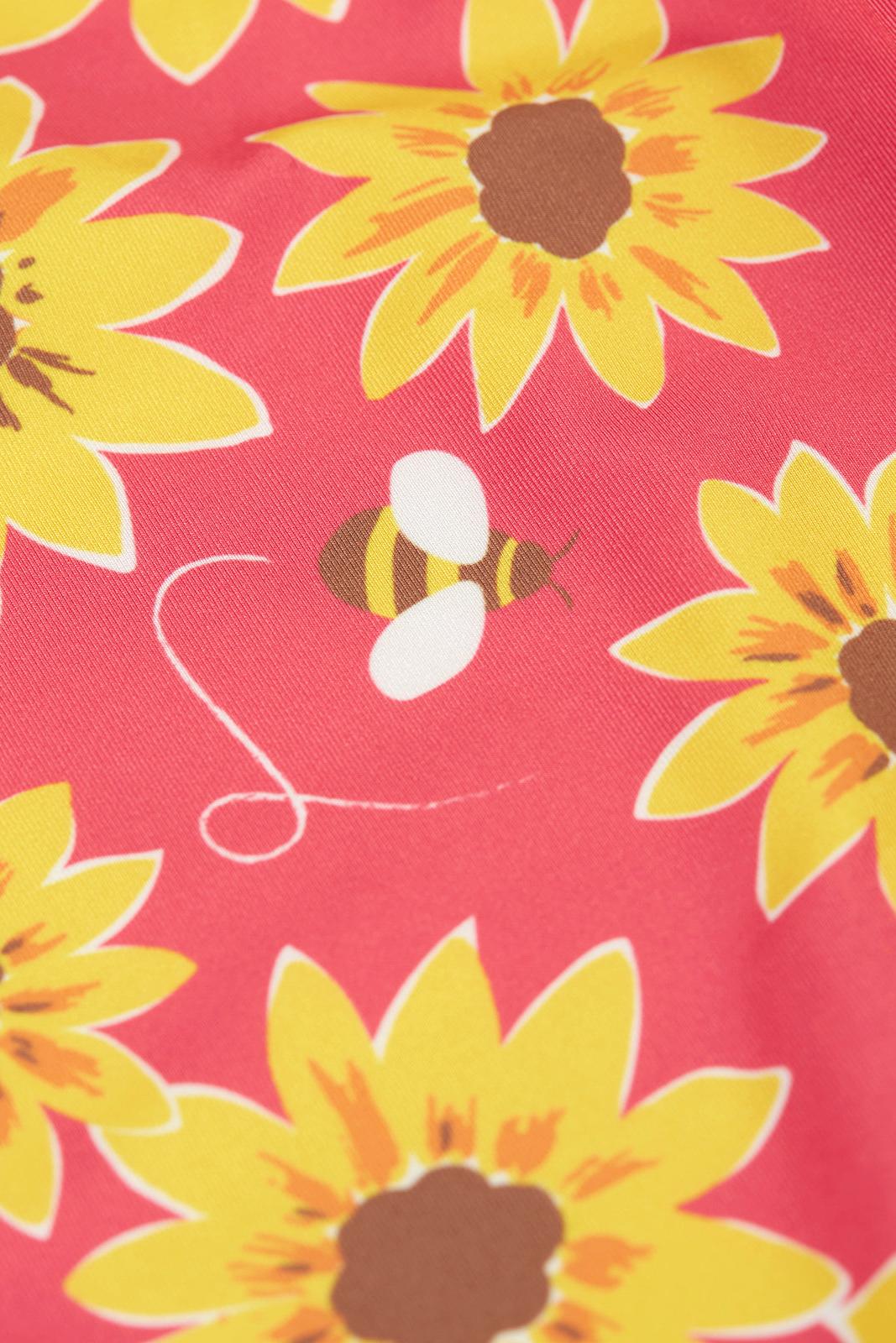 Close-up of Frugi fabric featuring a vibrant pink background with yellow sunflower illustrations and a small bee.