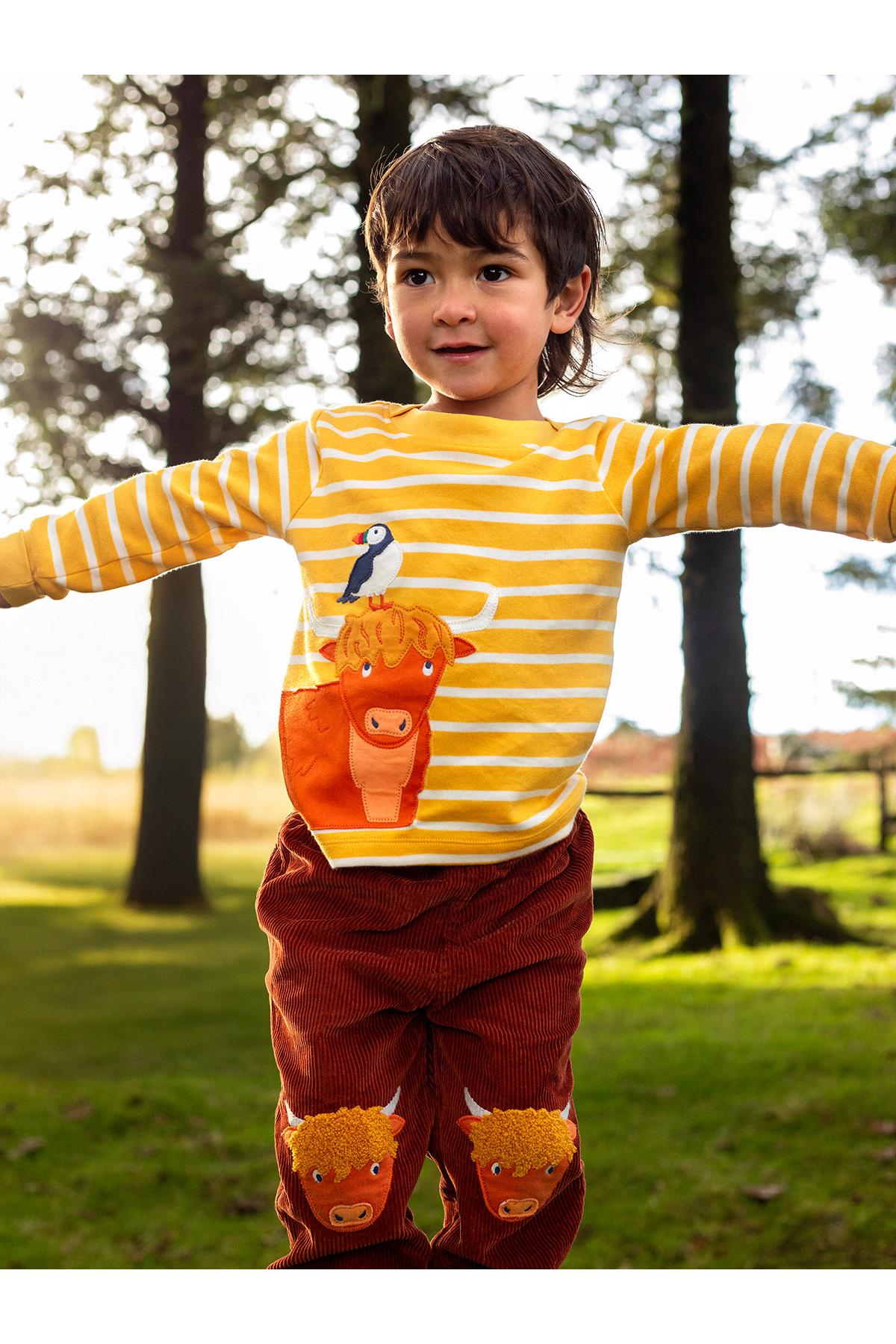 A child wearing a yellow striped Frugi organic cotton top with a highland cow and puffin applique design.