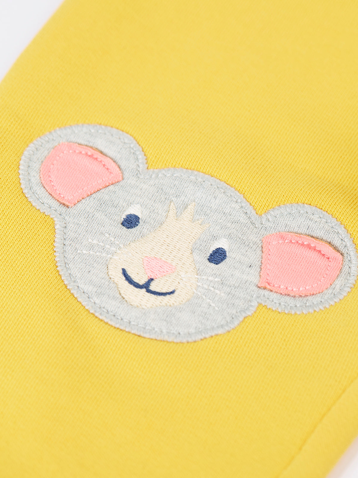 Close-up of a cute mouse applique on yellow organic cotton trousers.
