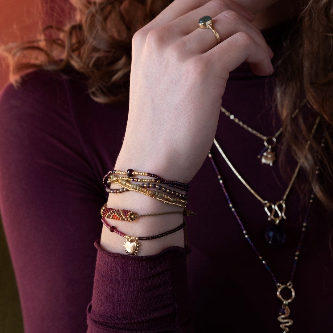 A close-up of a wrist wearing layered garnet gemstone bracelets with a golden heart charm.