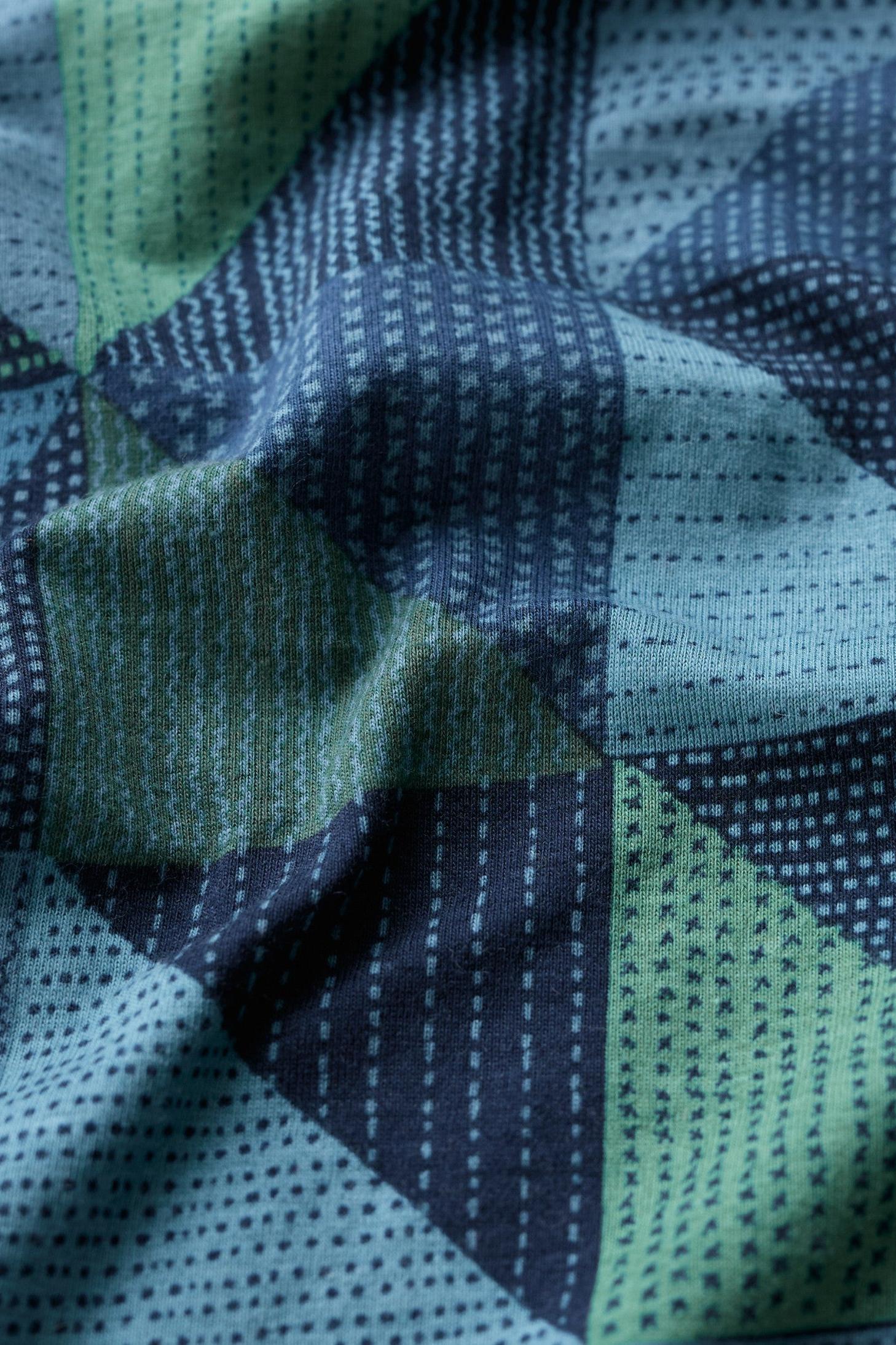 A close-up of a geometric patterned textile with stitched triangular sections in navy, light blue, and sage green, featuring dotted and dashed stripe motifs.