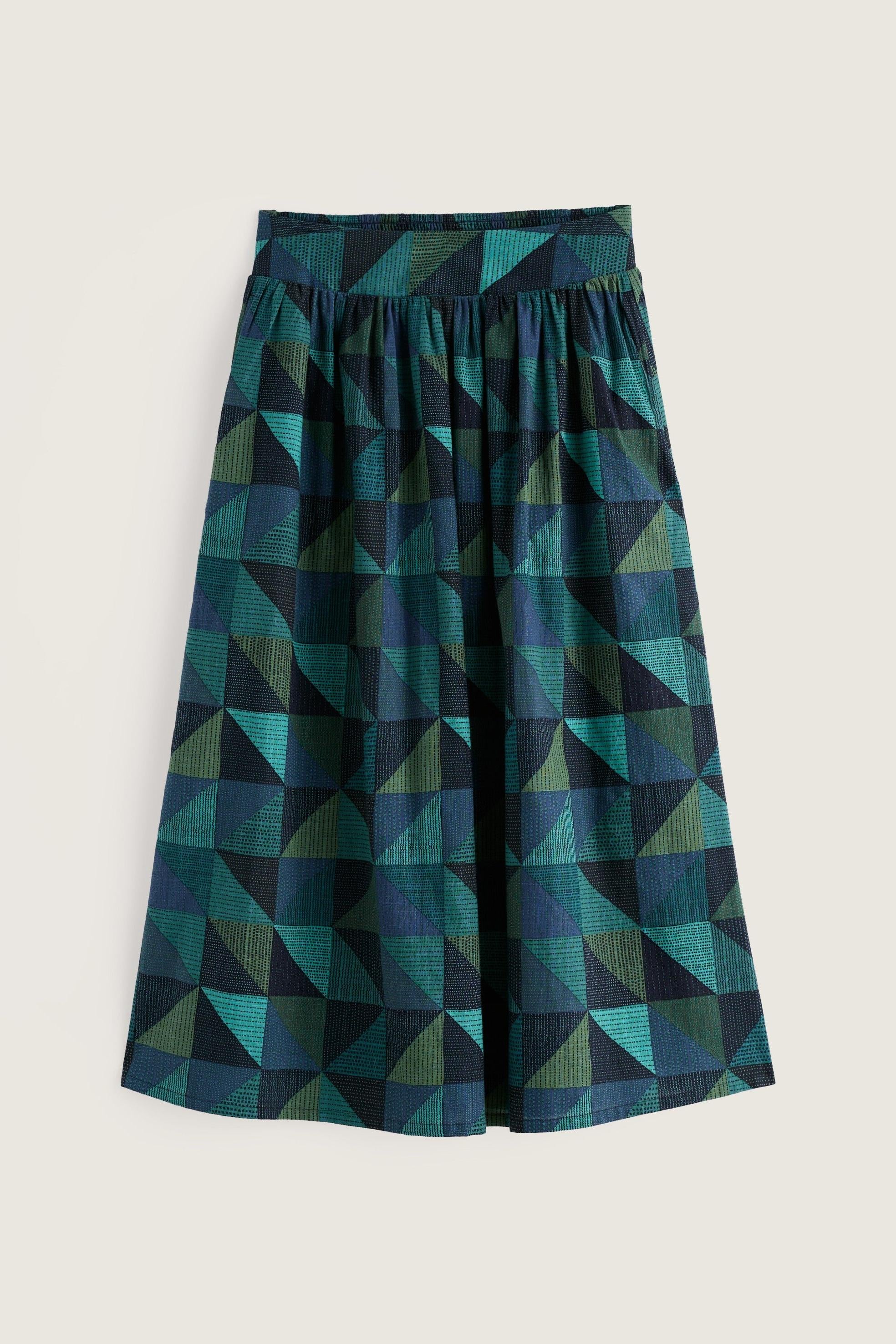 A pleated A-line skirt featuring a geometric triangle pattern in shades of teal, green, and dark navy blue, displayed against a solid light beige background.
