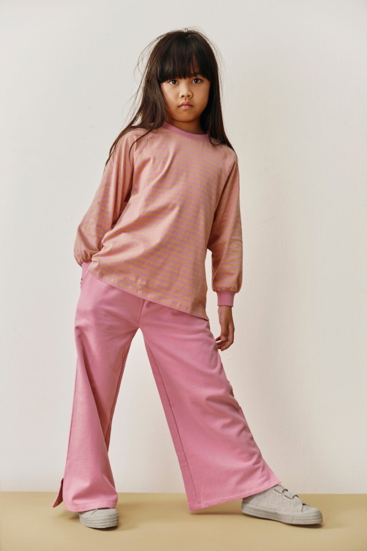 Child wearing a pink outfit standing against a plain background