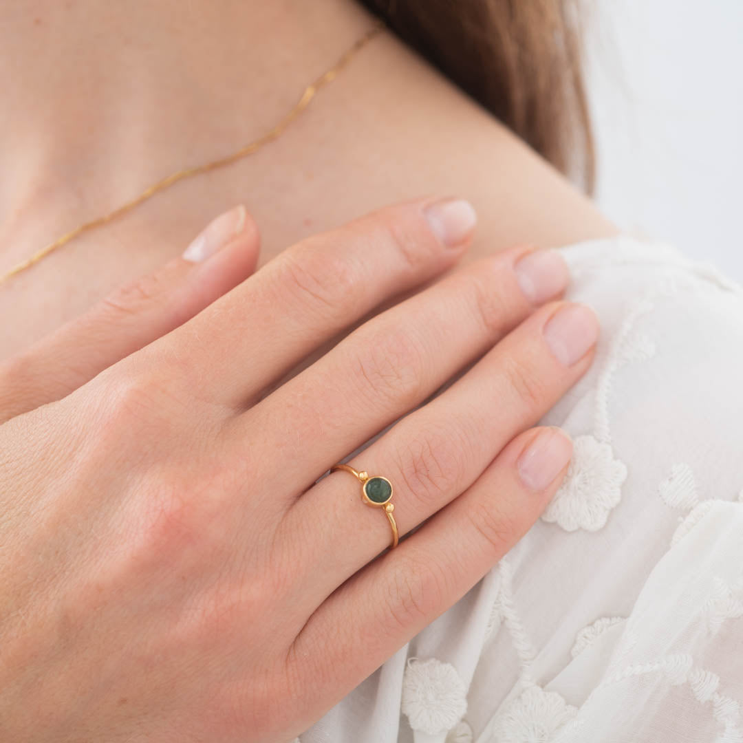 A woman wearing a delicate gold ring with a green aventurine gemstone on her finger.