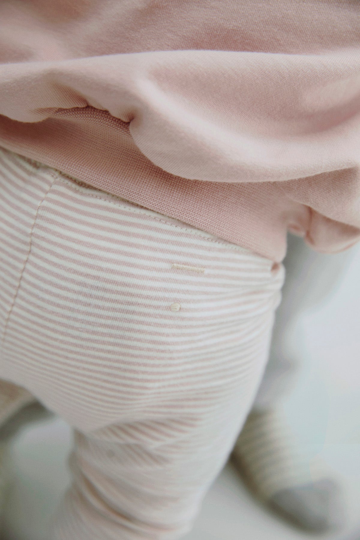 Close-up of a child wearing light pink ribbed pants and a pale pink top, with soft-focus background.