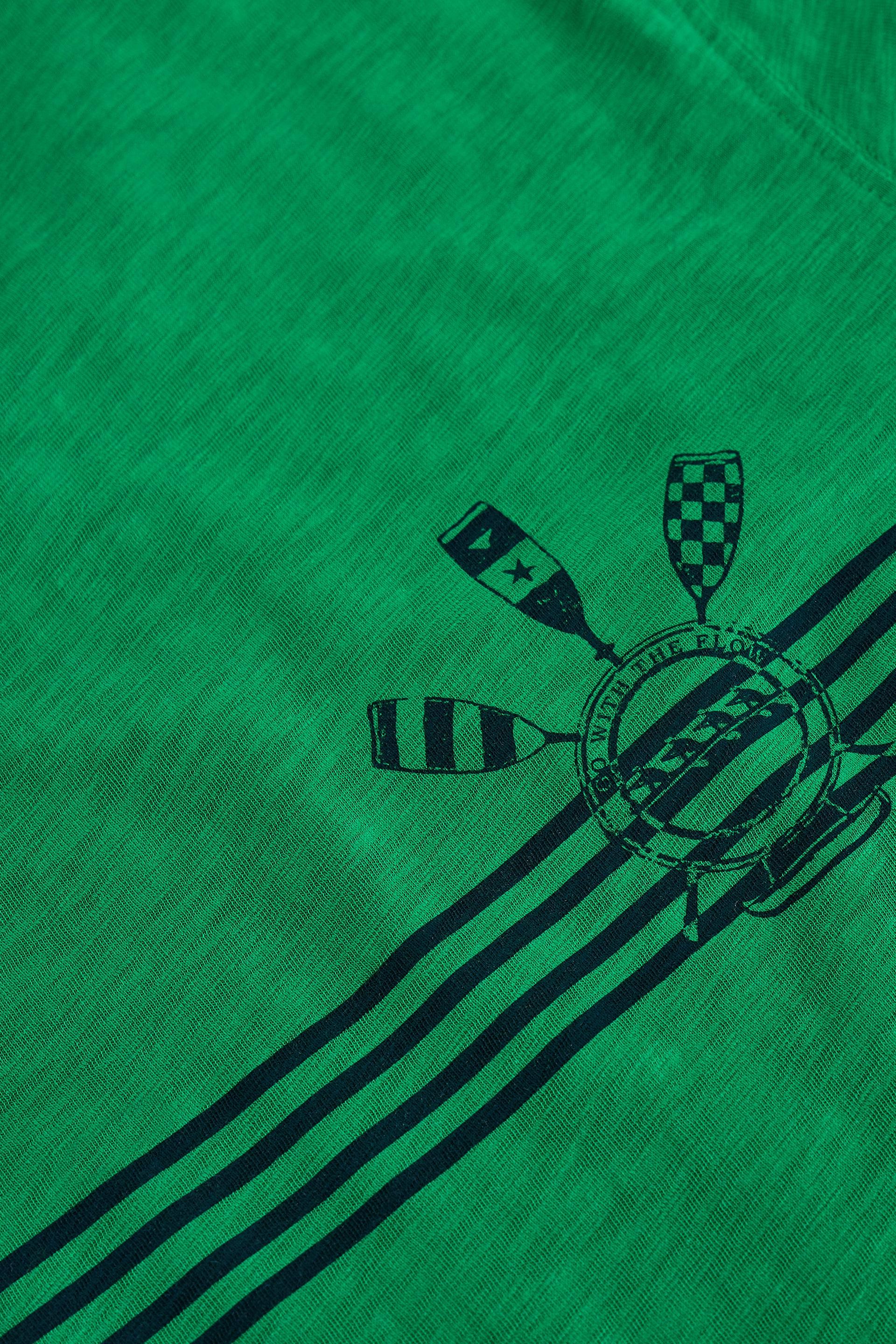 Close-up of a green t-shirt with a black printed crest featuring oars and stripes running diagonally across the fabric.