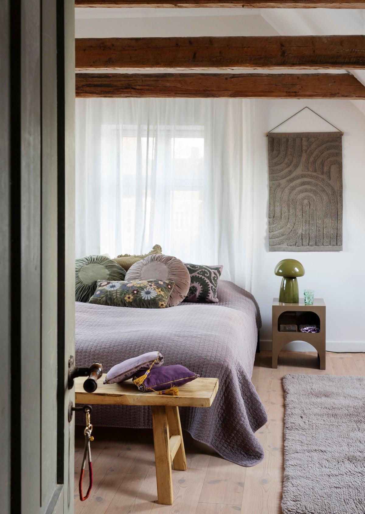 A cozy bedroom featuring a Madam Stoltz green velvet cushion and round cushions on a quilted bed.