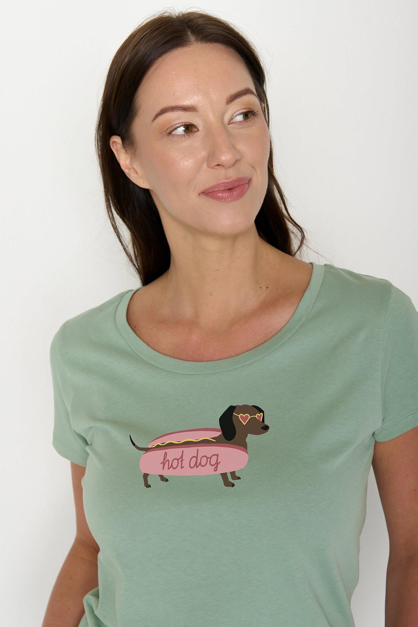 Woman wearing a green organic cotton t-shirt with a graphic of a dachshund on a hot dog and the text 'hot dog'.