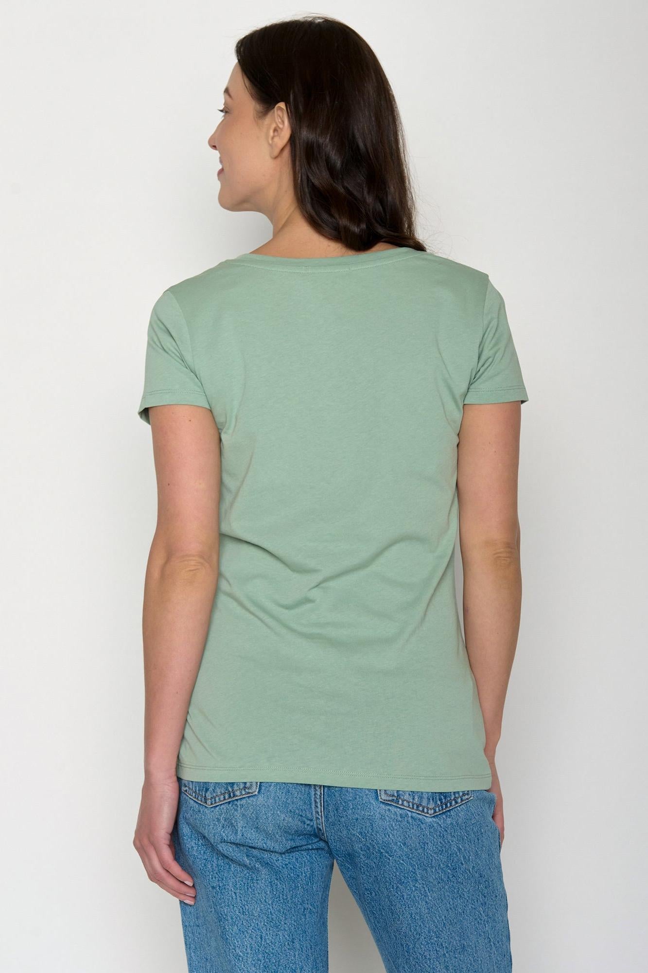 Person wearing a green organic cotton t-shirt and blue jeans against a white background