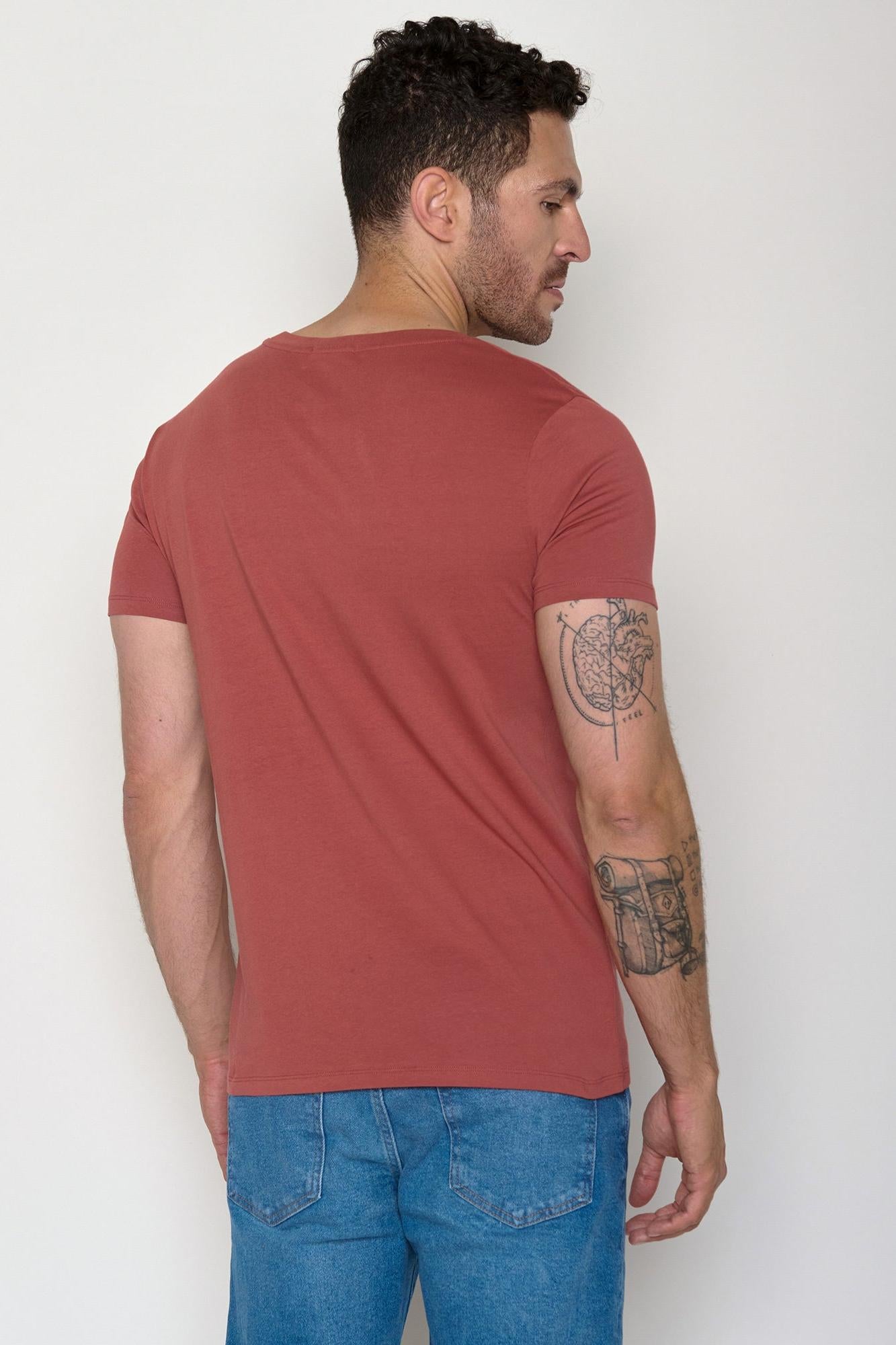 Man wearing a red organic cotton t-shirt and blue jeans against a white background