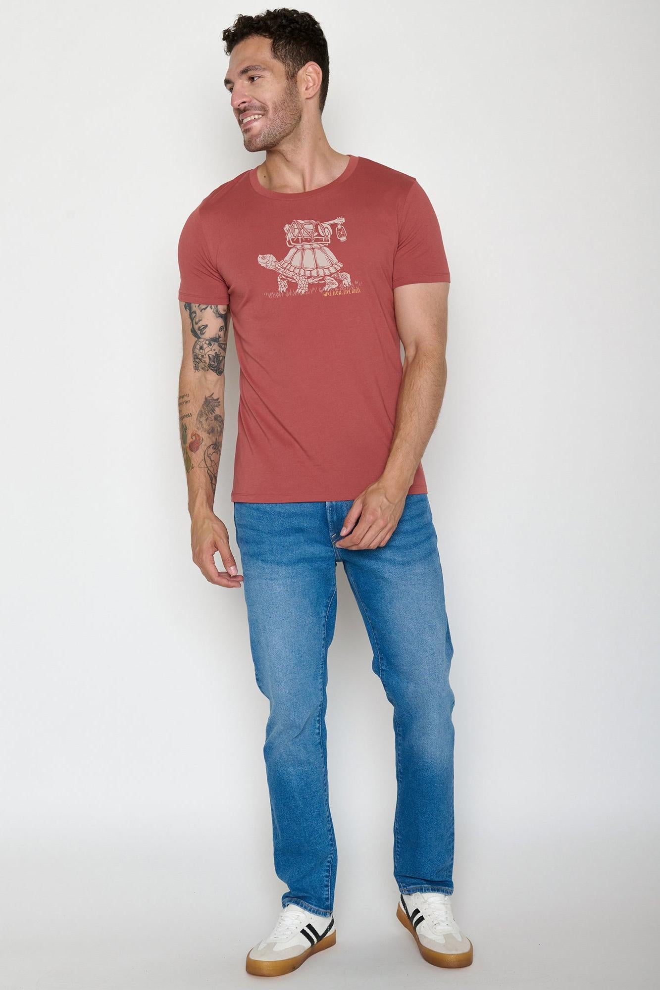 Man wearing a red t-shirt with a graphic design and blue jeans on a white background