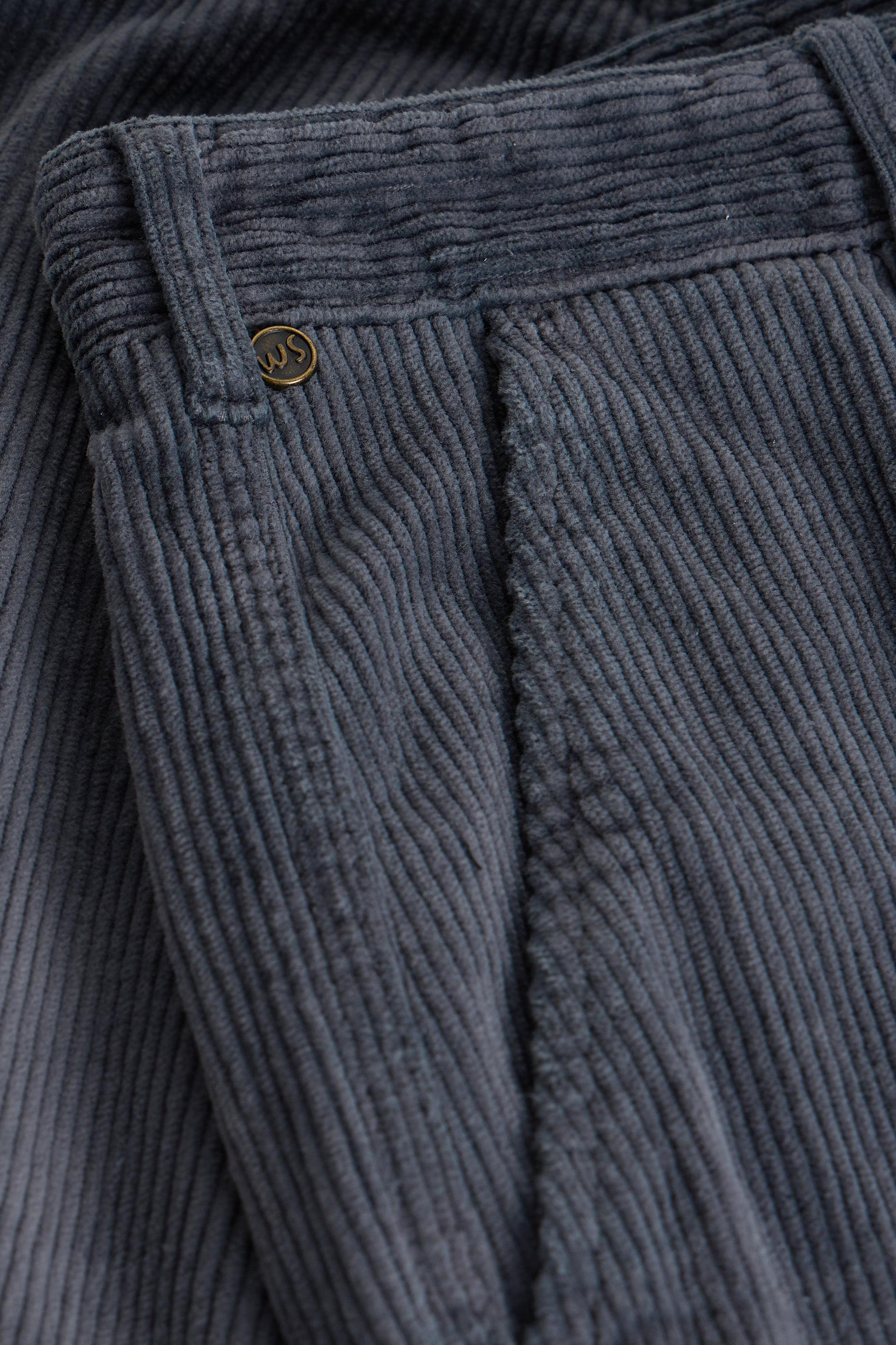 Close-up of dark gray corduroy trousers showing the ribbed texture, belt loops, and a small gold-toned button closure.