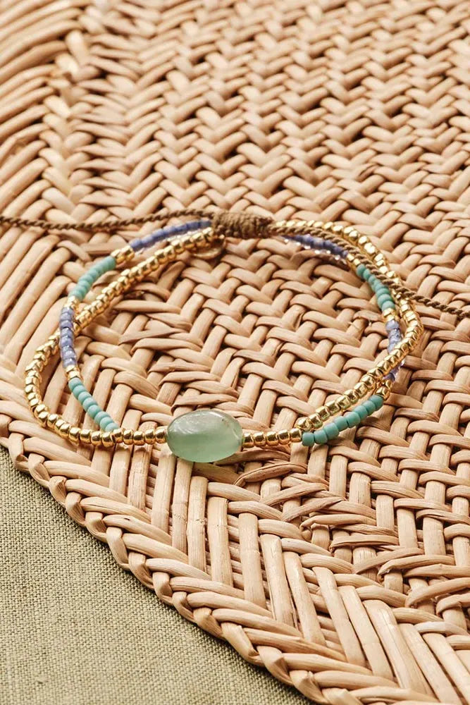 Gold bracelet with green stone on a woven mat
