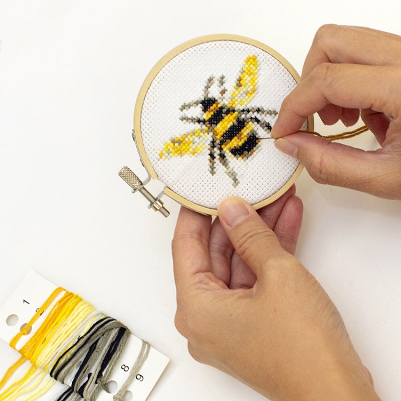 Close-up of hands stitching a mini bee embroidery project in a wooden hoop with thread organizer
