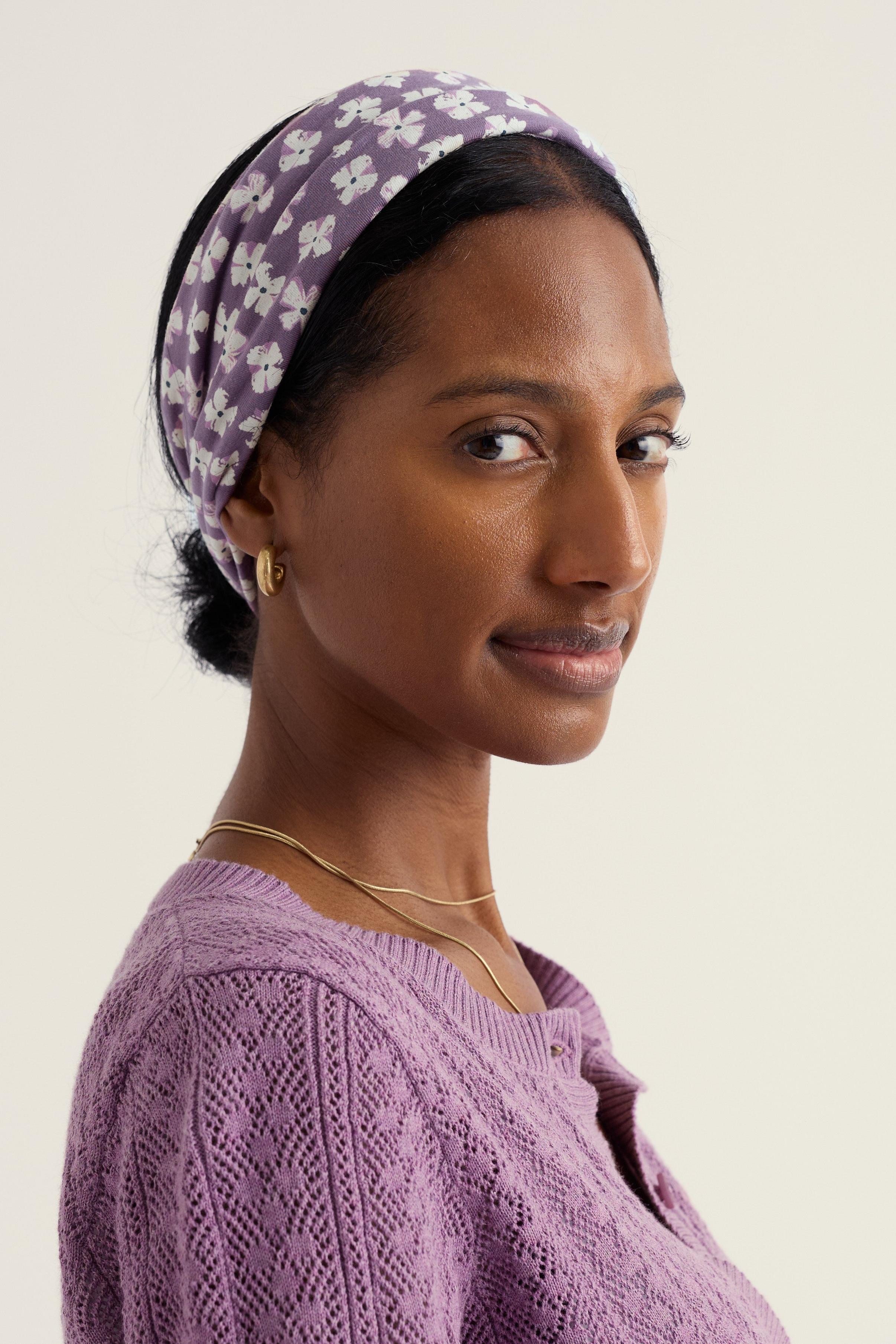 Woman wearing a purple patterned headscarf and matching sweater against a plain background