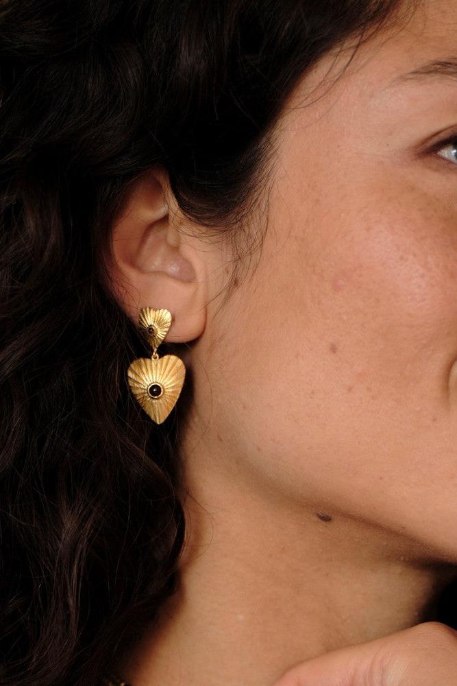 Woman wearing elegant heart-shaped gold plated earrings with a garnet gemstone.